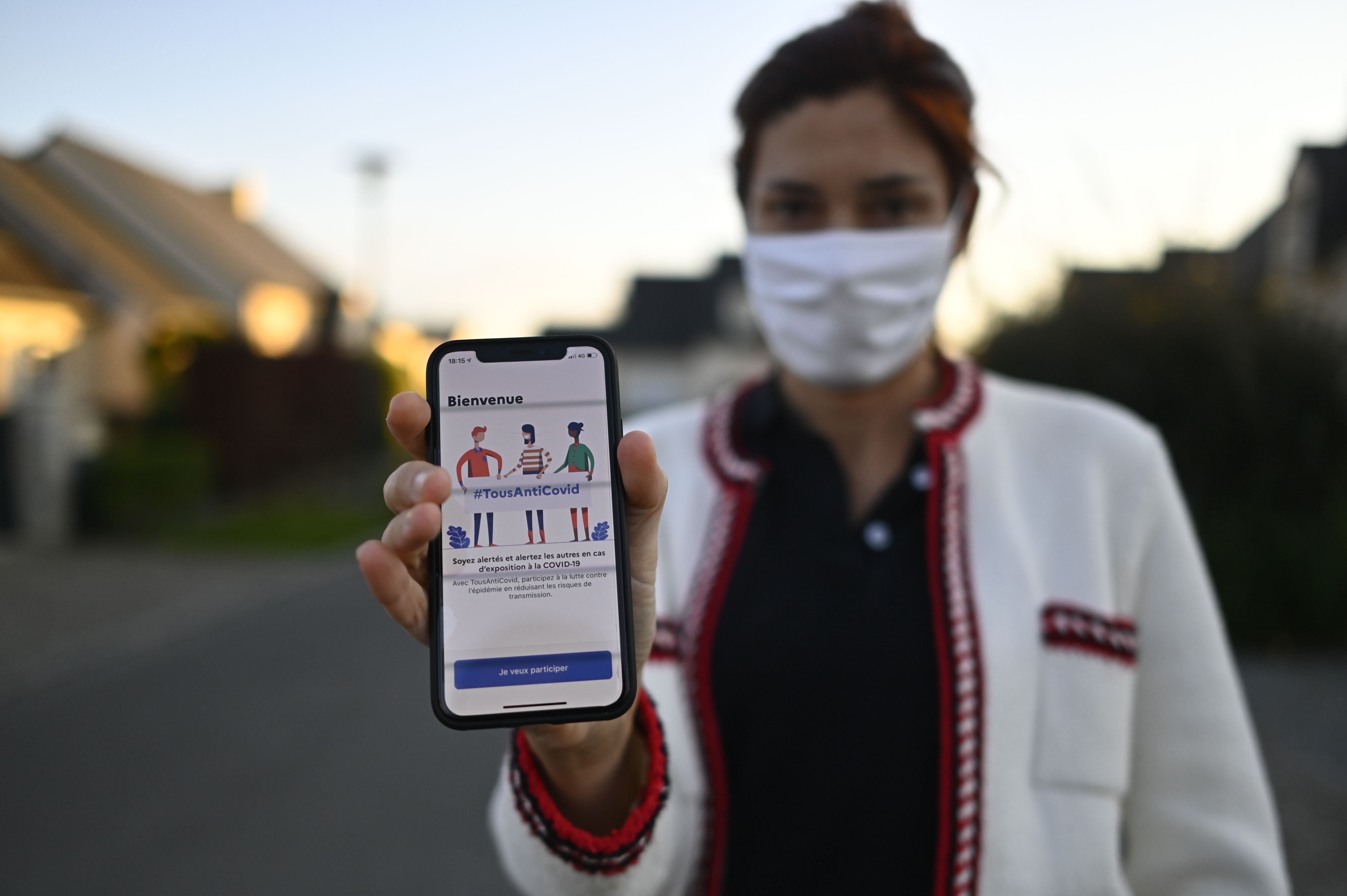 A woman wearing a face mask holds a smartphone showing the new "TousAntiCovid" application in Rennes, western France, on October 22, 2020, as several departments were put in "maximum alert" and new curfew measures put in place in order to curb the spread of the Covid-19 (the novel coronavirus). - The "StopCovid" contact tracing application, which has been controversial and little used since its release on June 2, has been relaunched on October 22 in a new form and renamed "TousAntiCovid". (Photo by DAMIEN MEYER / AFP)