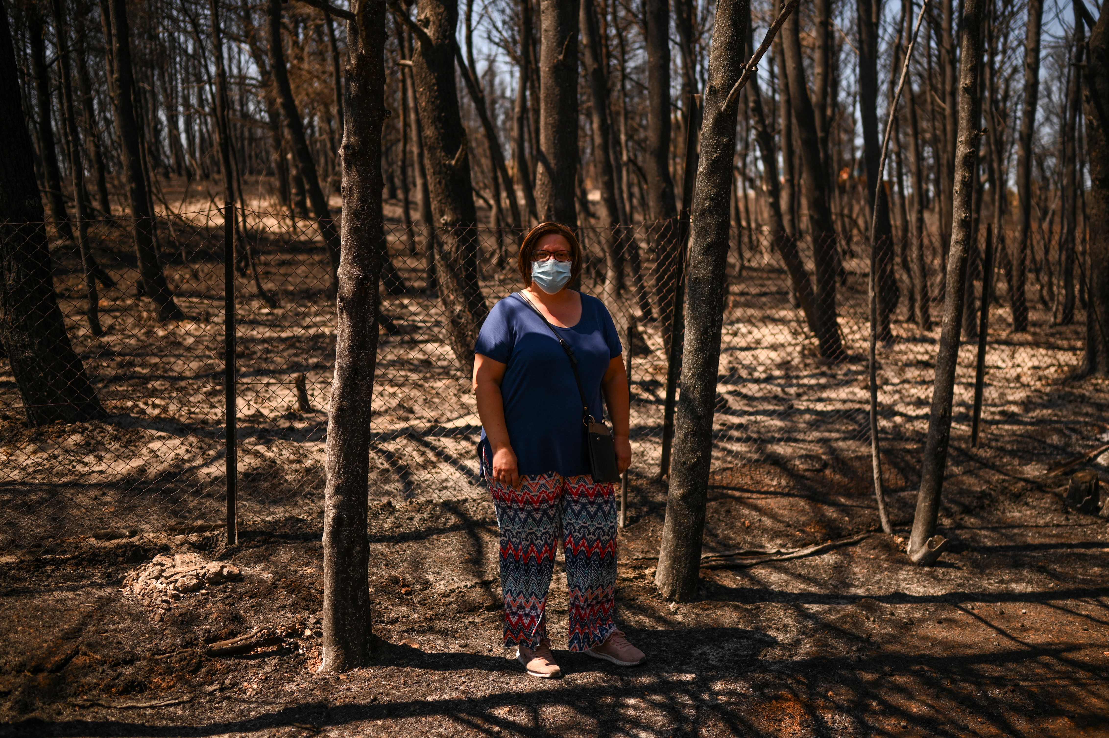 TOPSHOT - Eleni Haniosakis, 45 year-old, stands next to her burnt home in the village of Krioneri, north of Athens, on August 13, 2021. - Fires burning for more than a week that caused Greece's worst ecological disaster in decades were finally brought under control on August 13, 2021, the fire department said, as the government raced to fund reconstruction amid mounting anger. (Photo by Angelos Tzortzinis / AFP)