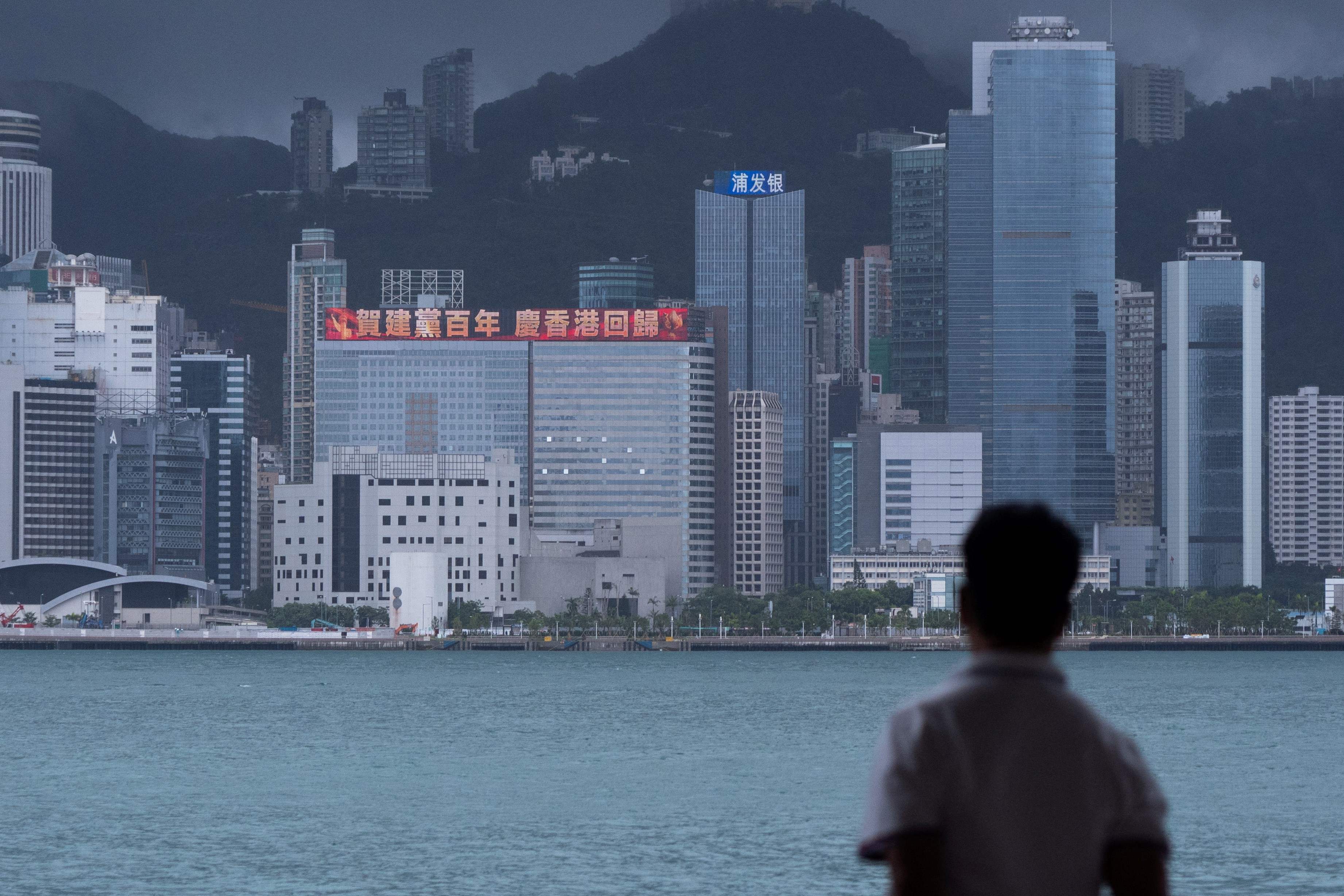 (FILES) In this file photo taken on June 29, 2021, a man looks at a building with a LED billboard displaying a slogan celebrating the 100th anniversary of the Chinese Communist Party and the 24th anniversary of Hong Kong�s return to China in Hong Kong. - This month was the first time high-profile events had been put on for the Chinese Communist Party (CCP) anniversary in Hong Kong. (Photo by Bertha WANG / AFP) / TO GO WITH HongKong-China-politics,FOCUS