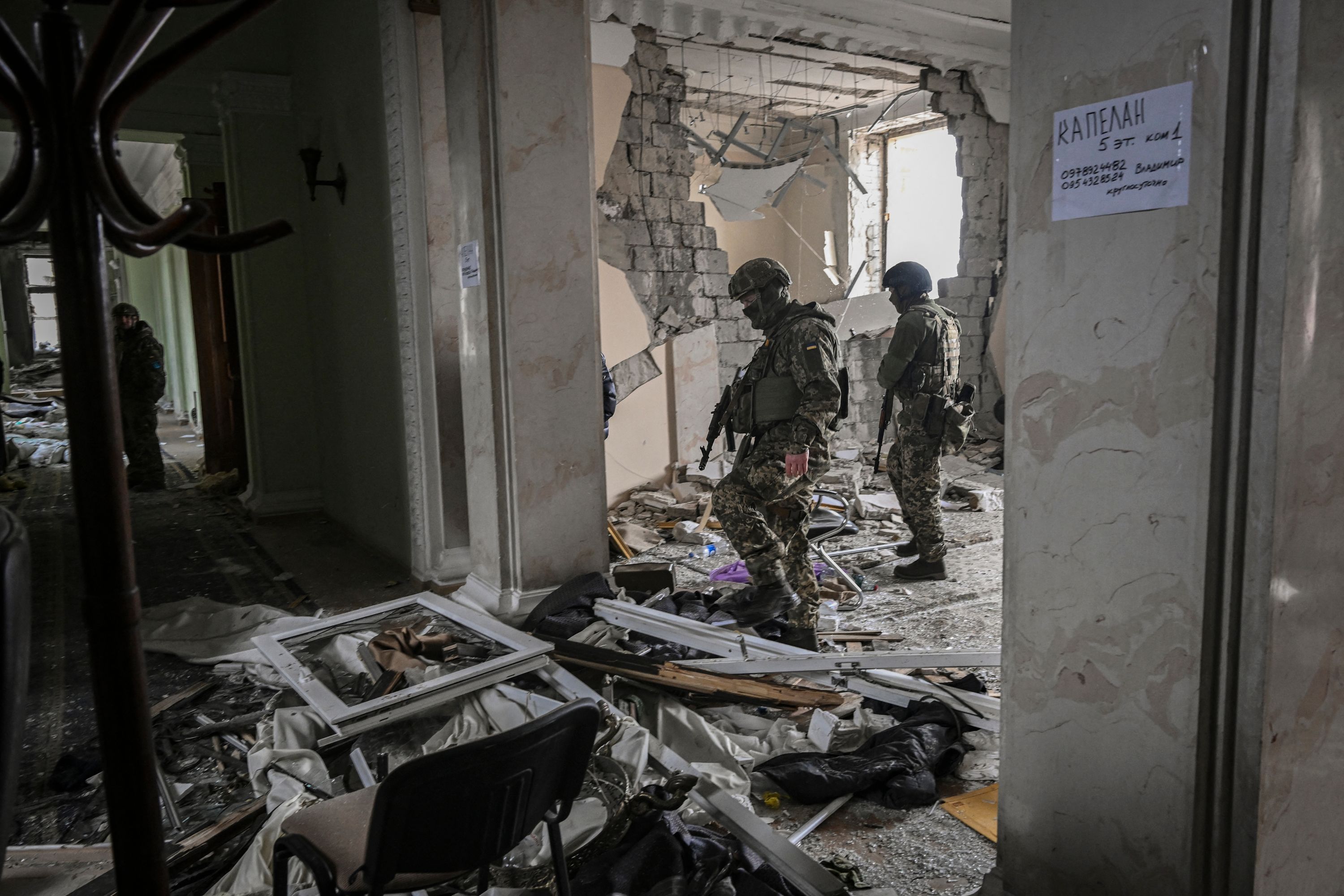 TOPSHOT - Ukranian servicemen walk inside the destroyed regional headquarters of Kharkiv on March 27, 2022. - France's President Emmanuel Macron has warned against a verbal "escalation" of Russia's invasion in Ukraine, after US President Joe Biden branded Vladimir Putin a "butcher" who "cannot remain in power".In Kharkiv, where authorities reported 44 artillery strikes and 140 rocket assaults in a single day, residents were resigned to the incessant bombardments. (Photo by Aris Messinis / AFP)