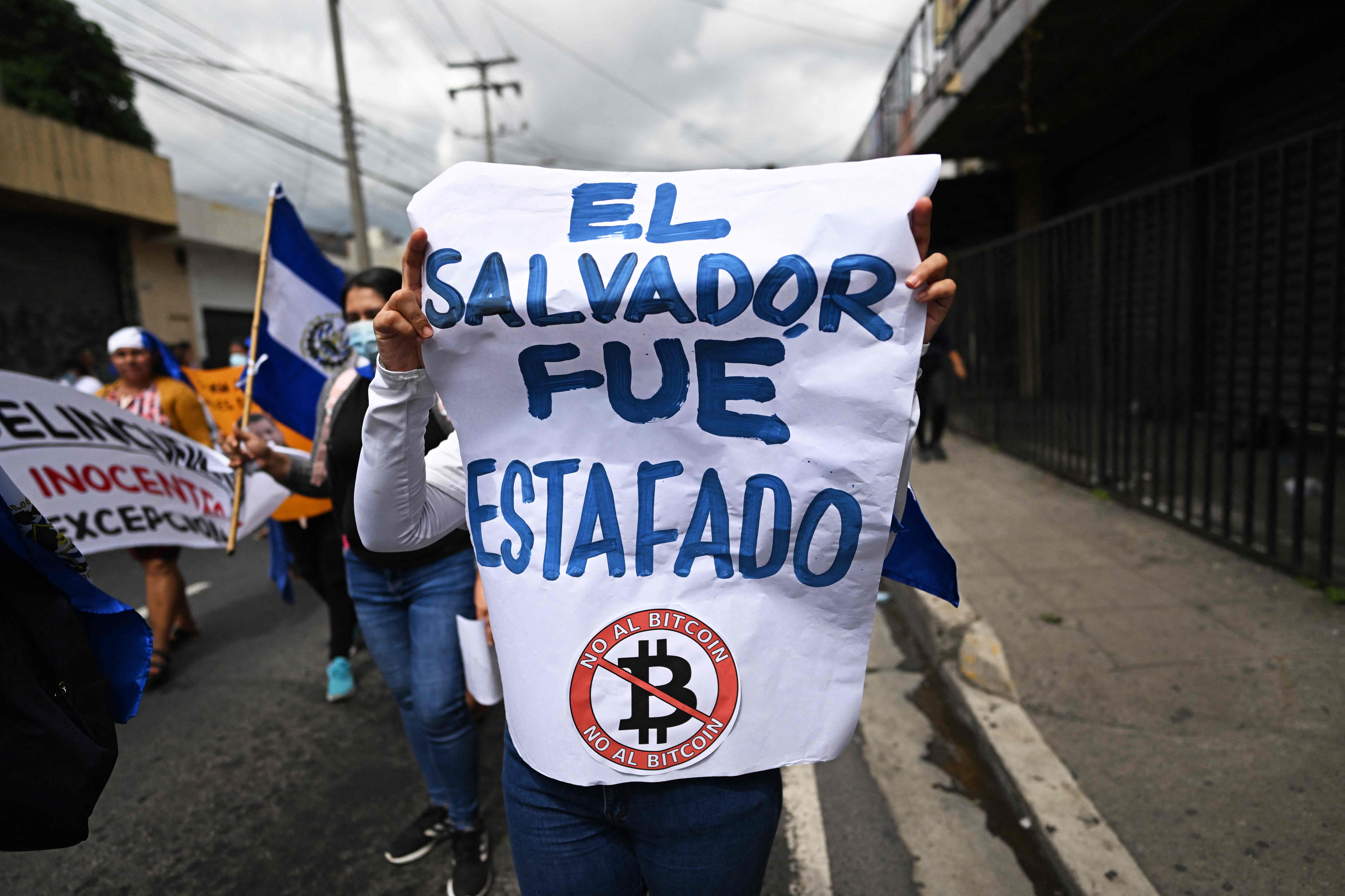 An opposer to the government of Salvadoran President Nayib Bukele holds a poster that reads "El Salvador was scammed" during a demonstration to protest against Bukele's security policies, during El Salvador's 201st anniversary of independence in San Salvador, on September 15, 2022. (Photo by Marvin RECINOS / AFP)