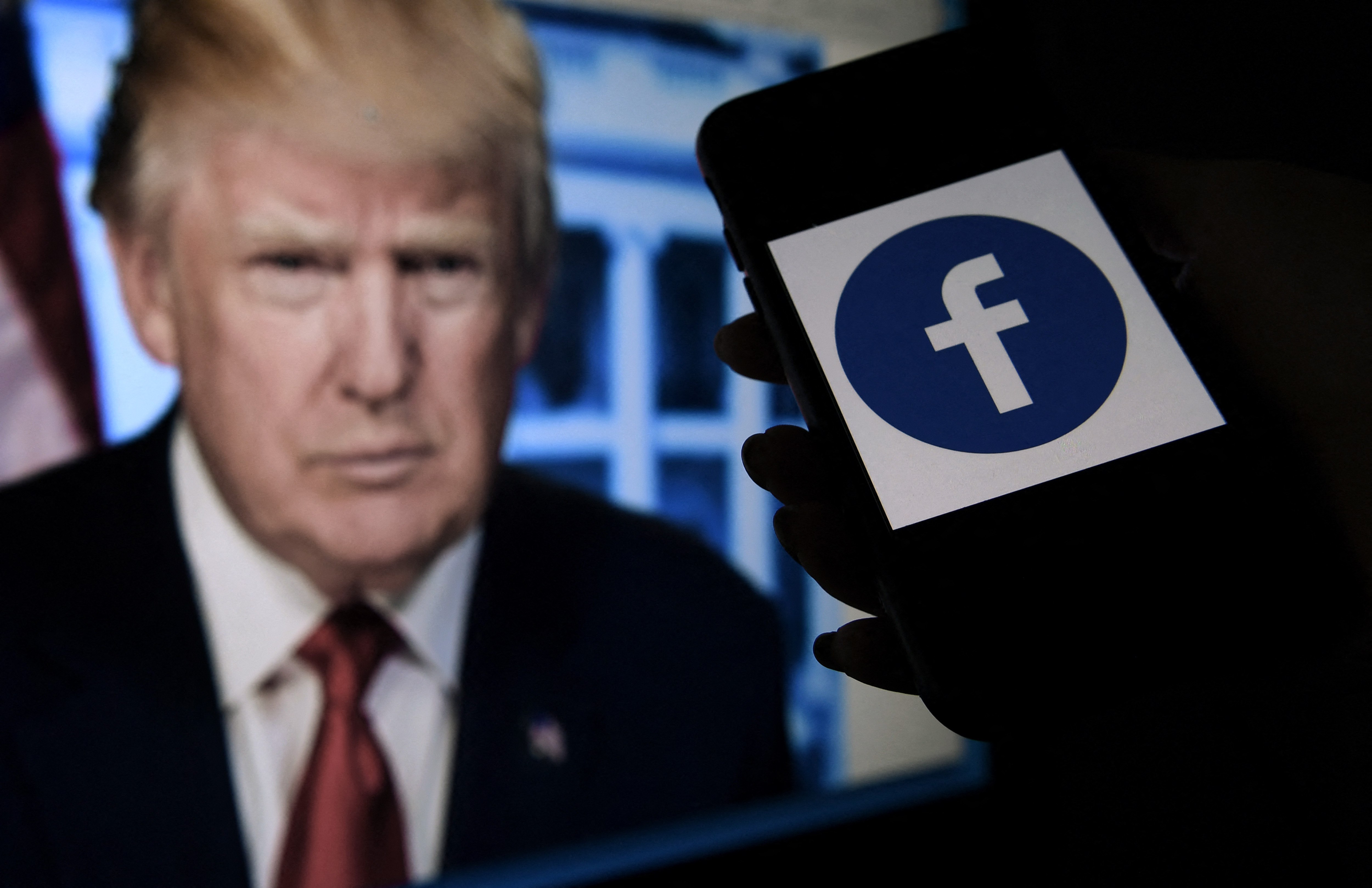En esta foto de ilustración de archivo tomada el 4 de mayo de 2021, la pantalla de un teléfono muestra un logotipo de Facebook con el retrato oficial del expresidente de los Estados Unidos Donald Trump en el fondo en Arlington, Virginia.