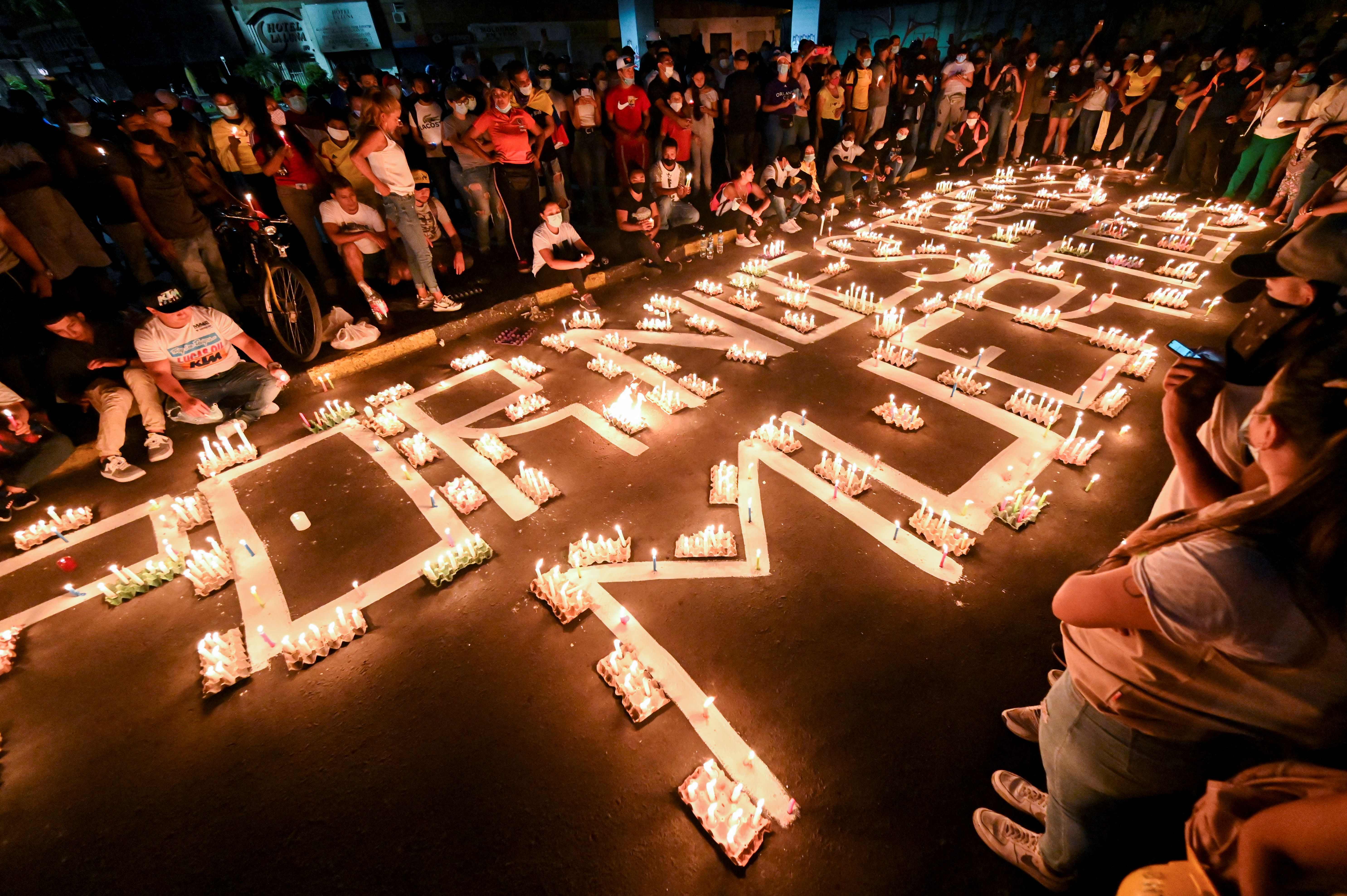 People gather around candles and words on the pavement reading "for our dead" during a vigil on May 5, 2021 in Cali, Colombia, in honor of the demonstrators who died during protests against the government of President Ivan Duque. - Thousands of people returned to the streets of Colombia on May 5 in rejection of the government of Ivan Duque, who has completed a week of pressure with demonstrations that turned violent in some cities and left some twenty people dead. (Photo by Luis ROBAYO / AFP)