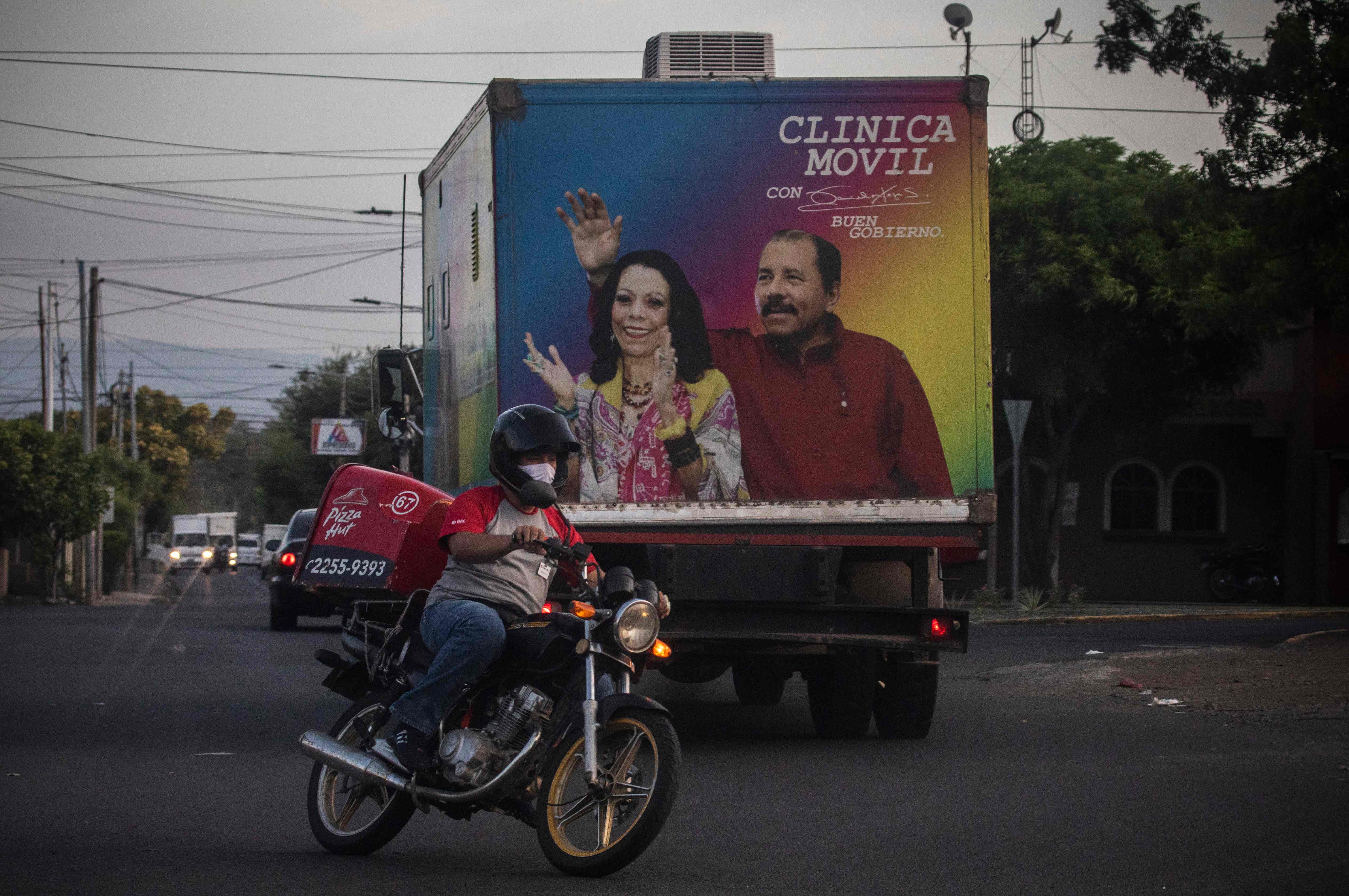 A byker drives pass a mobile clinic of the Ministry of Health with the image of Nicaraguan President Daniel Ortega and his wife Rosario Murillo in Managua on May 18, 2020. - Nicaragua's government announced the closure of borders with Costa Rica after Costa Rican authorities began to restrict the entry of cargo trucks through its border on Monday to contain the spread of COVID-19. (Photo by INTI OCON / AFP)