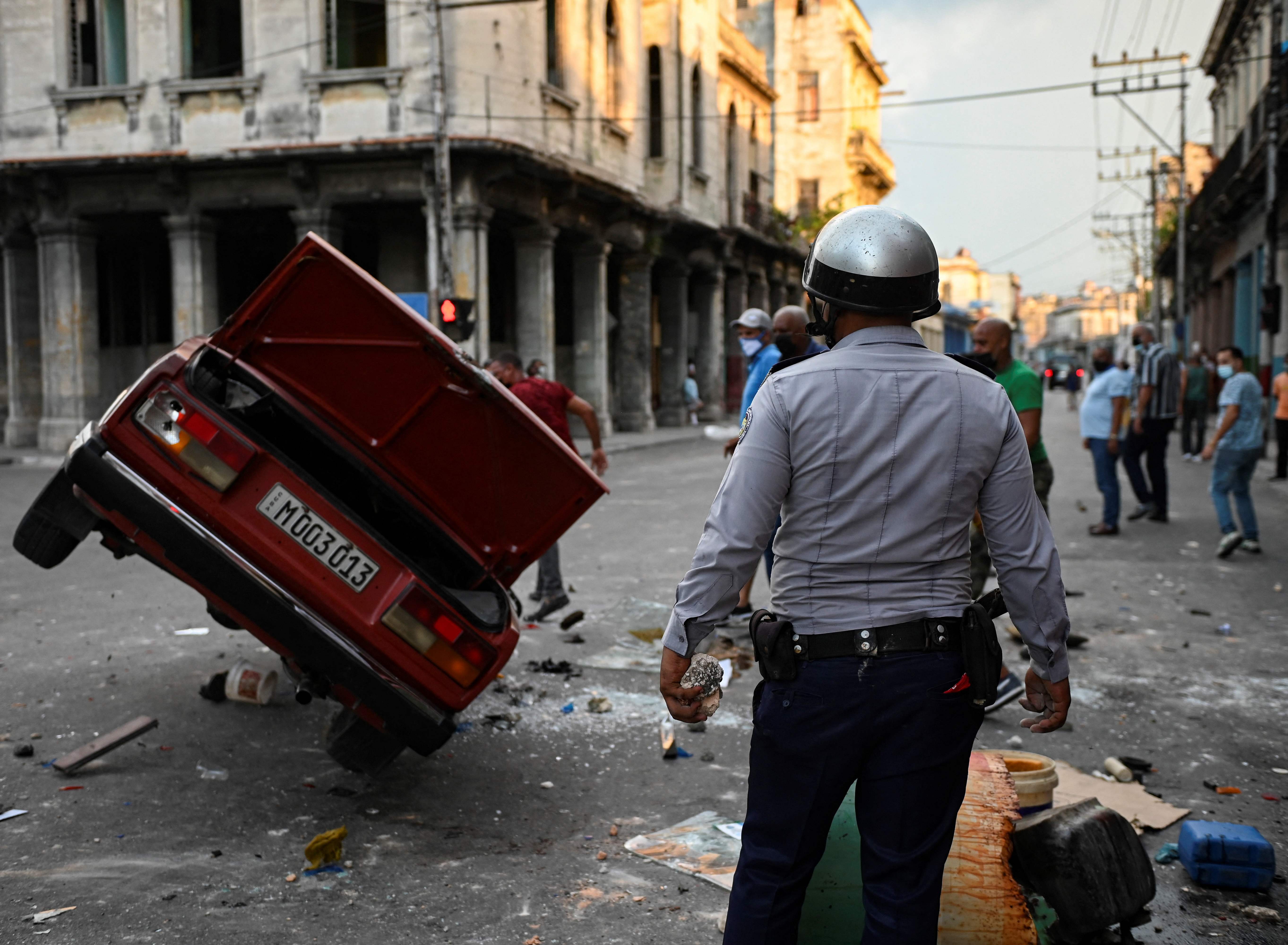 A policeman stands while watching a police car overturned in the street in the framework of a demonstration against Cuban President Miguel Diaz-Canel in Havana, on July 11, 2021. - Thousands of Cubans took part in rare protests Sunday against the communist government, marching through a town chanting "Down with the dictatorship" and "We want liberty." (Photo by YAMIL LAGE / AFP)