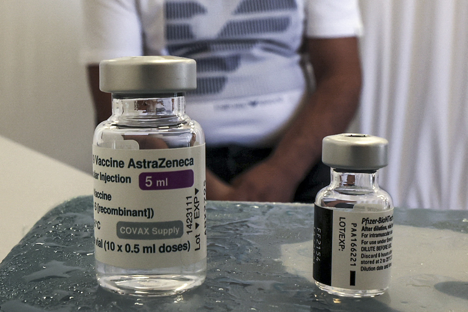 A man sits behind two vials of the (L to R) Oxford-AstraZeneca and Pfizer BioNTech COVID-19 coronavirus vaccines at a vaccination centre in the city of Ramallah in the occupied West Bank on August 19, 2021. (Photo by ABBAS MOMANI / AFP)
