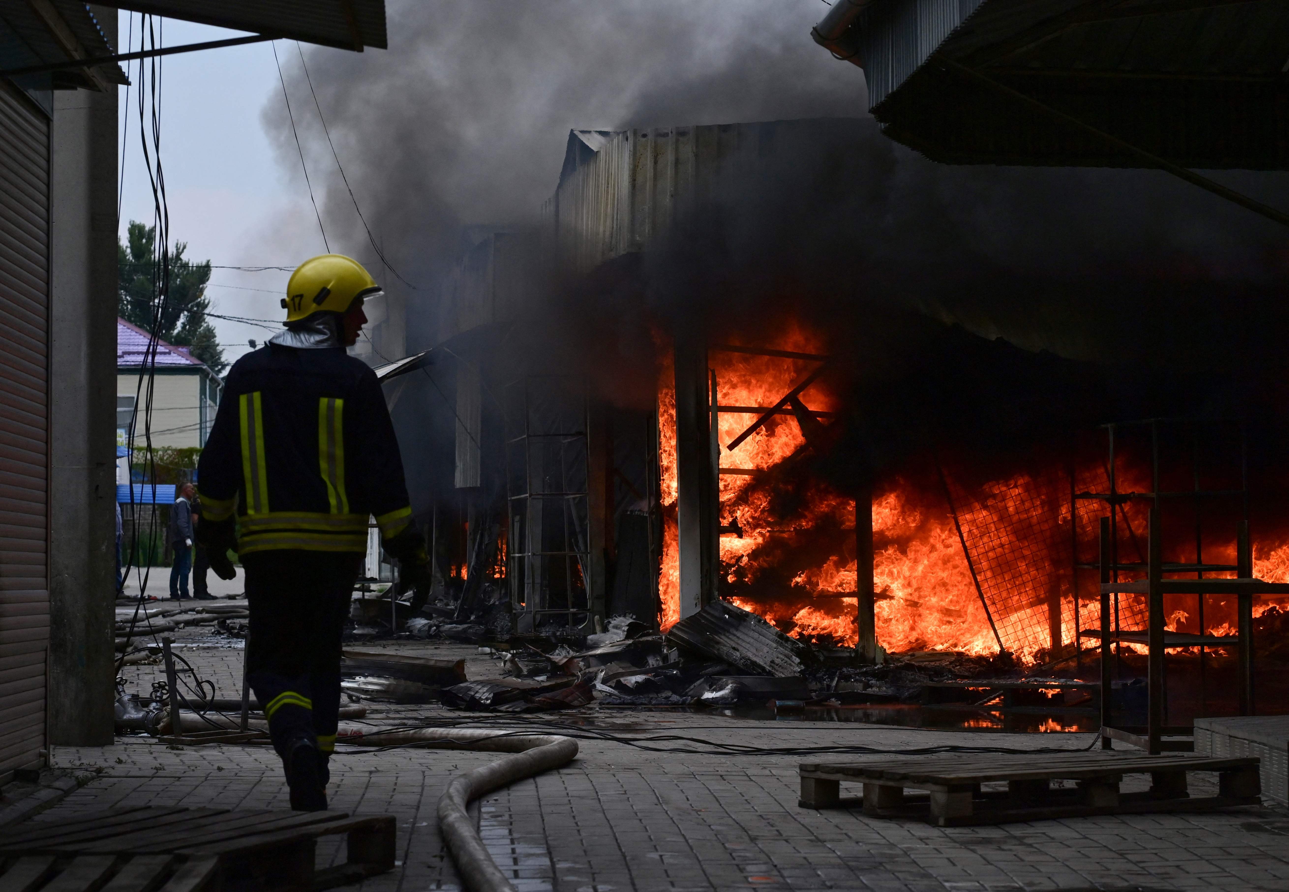 A firefighter works with colleagues to control flames at the central market of Sloviansk on July 5, 2022, following a suspected missile attack amid the Russian invasion of Ukraine. (Photo by MIGUEL MEDINA / AFP)