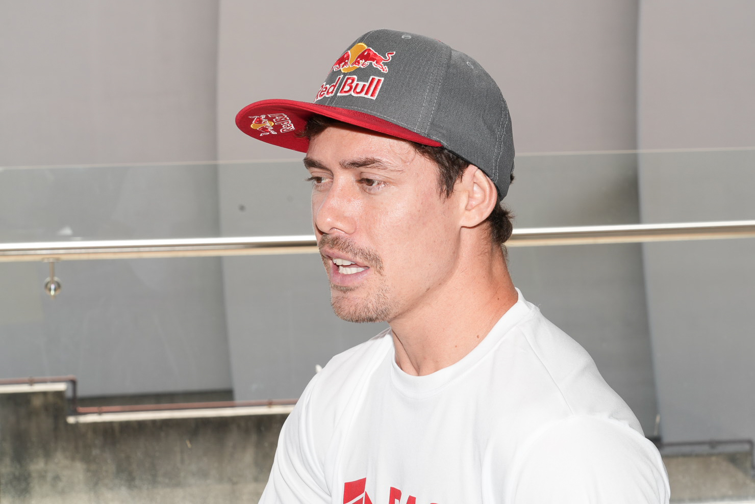 El ciclista Kenneth Tencio en una conferencia de prensa. Sostiene un micrófono, usa gorra gris y camiseta blanca.