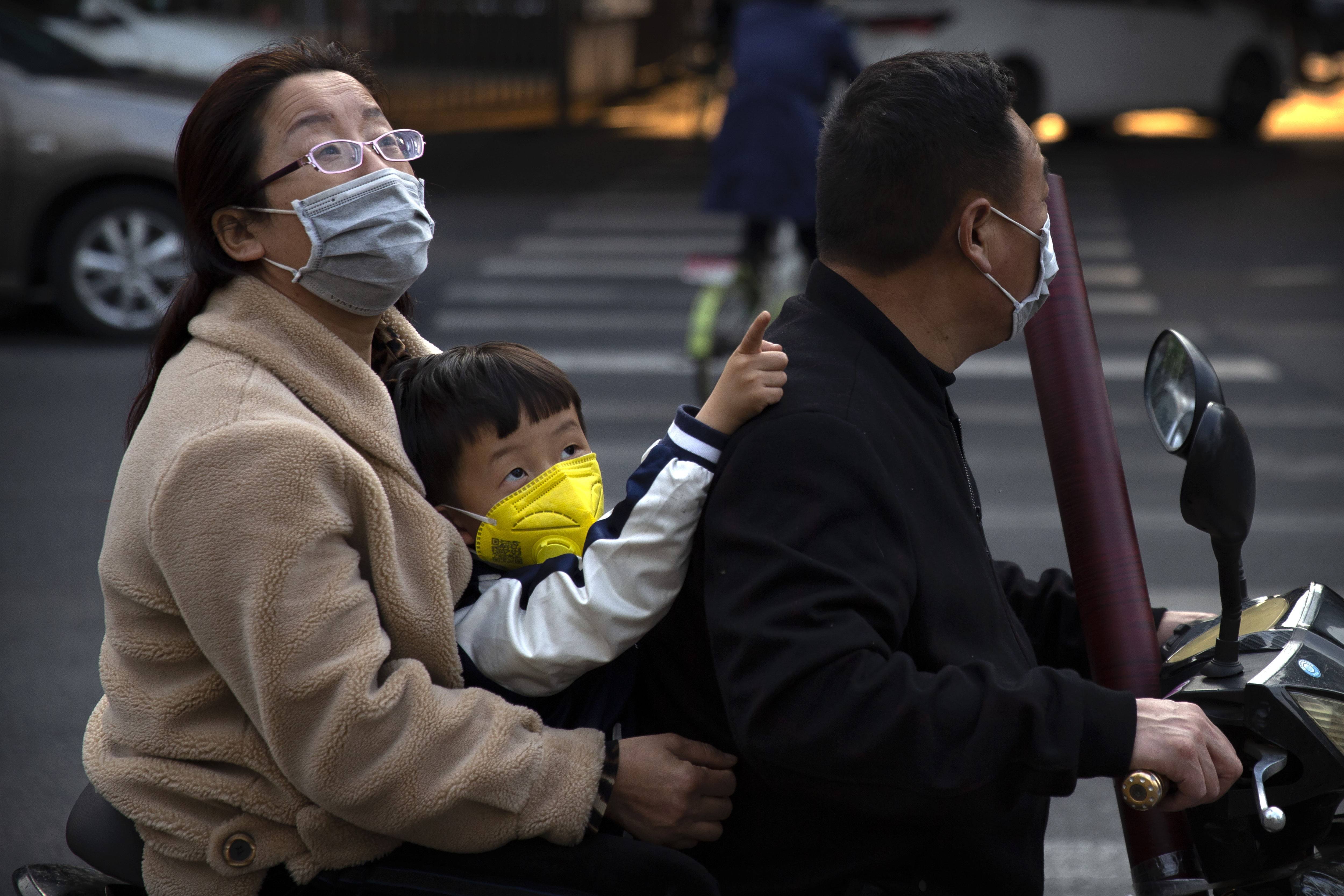 A boy wearing a face mask gestures as he sits on the back of a motor scooter in Beijing, Friday, April 17, 2020. China faces a drawn-out struggle to revive an economy that suffered its biggest contraction since possibly the mid-1960s after millions of people were told to stay home to fight the coronavirus. (AP Photo/Mark Schiefelbein)