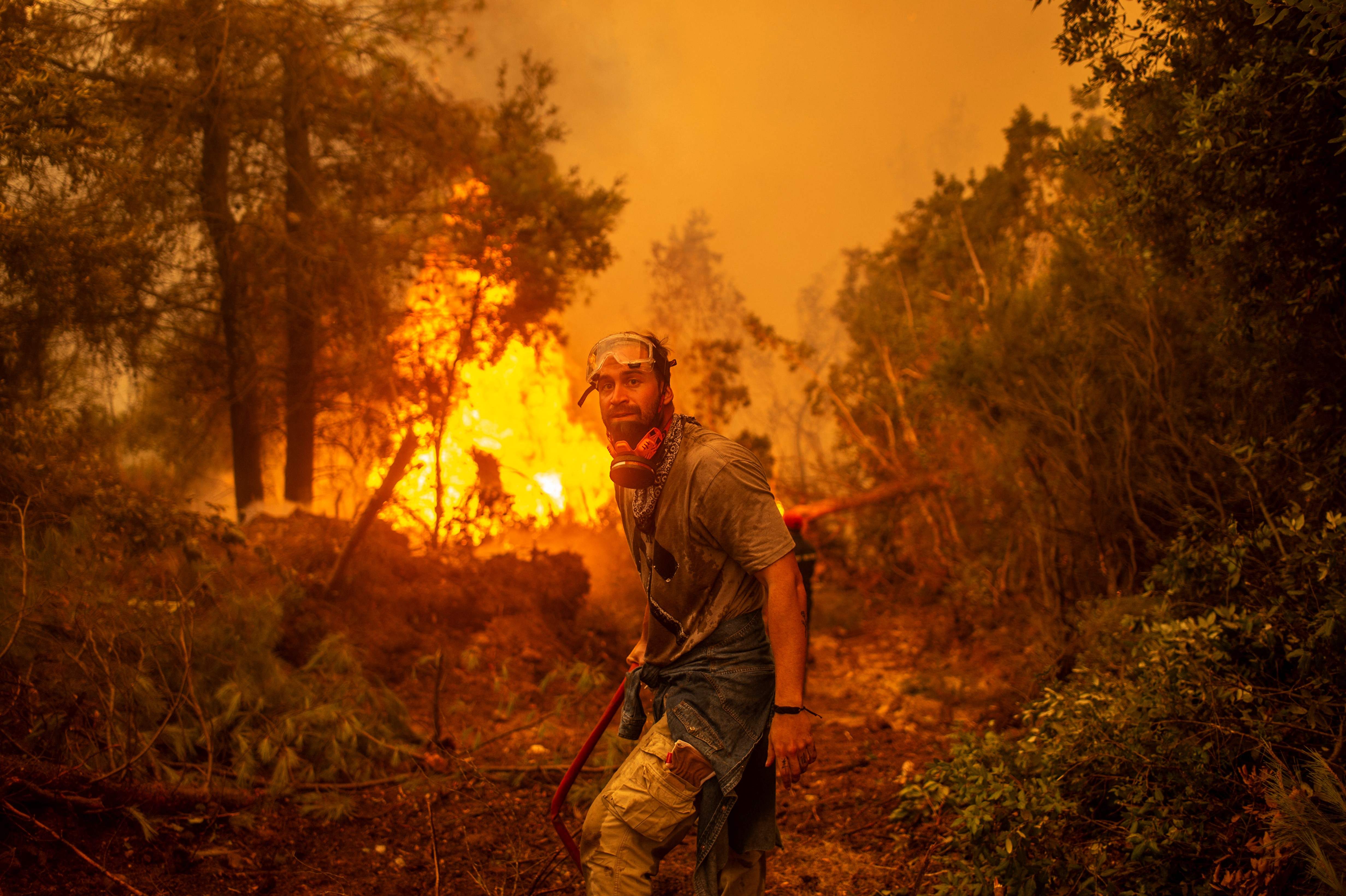 A volunteers holds a water hose near a burning blaze as he tries to extinguish a fire in the village of Glatsona on Evia (Euboea) island, on August 9, 2021. - Firefighters tried on August 9, to prevent fires from reaching key communities and a thick forest that could fuel an inferno that one official said has destroyed hundreds of homes in seven days on the Greek island of Evia. If most of nearly two weeks of fires had stabilised or receded in other parts of Greece, the ones on rugged and forested Evia were the most worrying and created apocalyptic scenes. (Photo by ANGELOS TZORTZINIS / AFP)