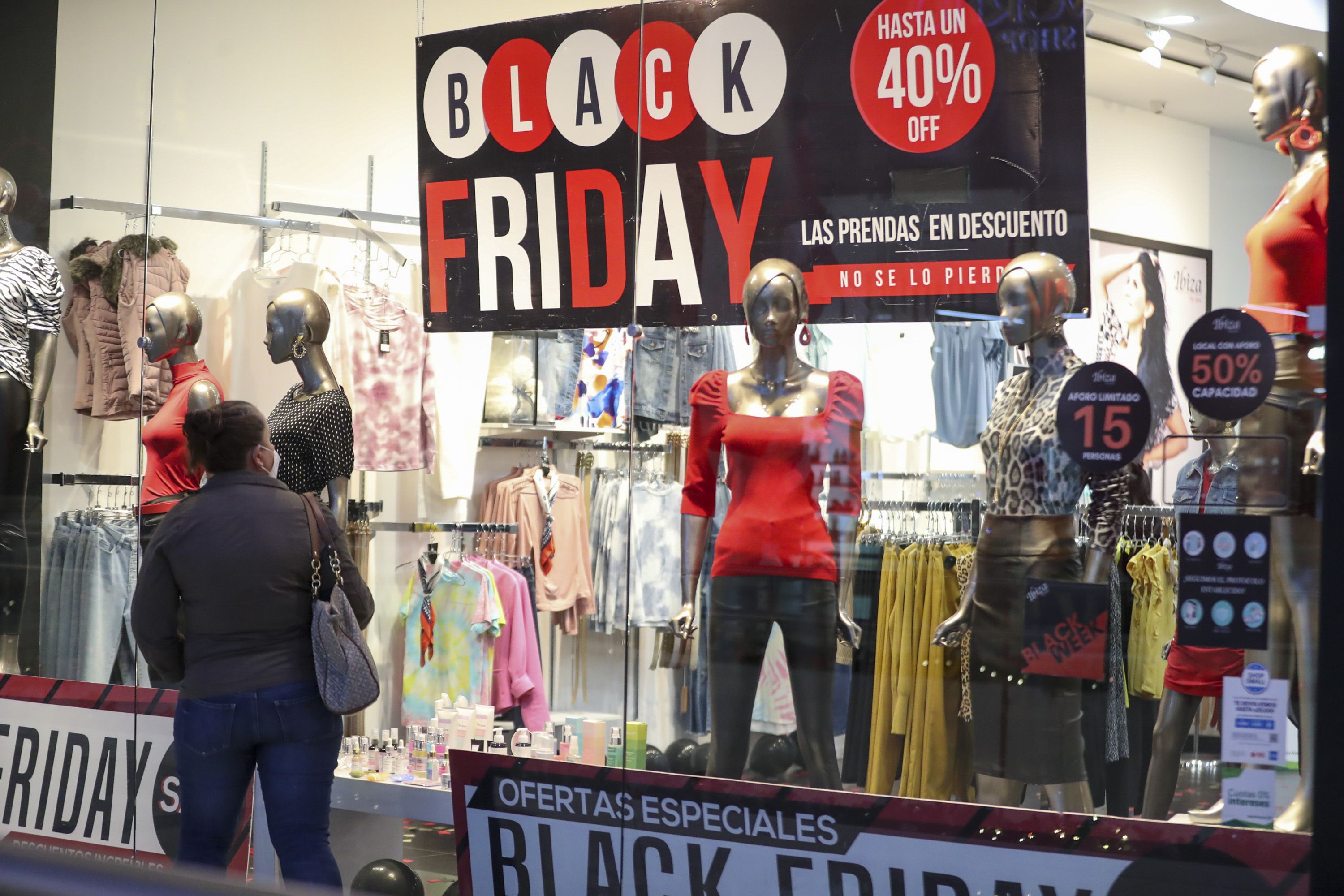 Mujer frente a un escaparate de tienda con maniquíes y un cartel que anuncia descuentos de Black Friday, con ofertas de hasta un 40% de descuento.