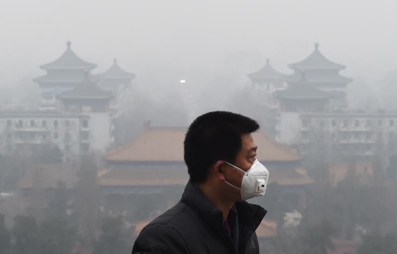 TOPSHOT - A man wears a mask to protect himself from air pollution in Beijing on December 8, 2015. Half of Beijing's private cars were ordered off the streets on December 8 and many construction sites and schools were closed under the Chinese capital's first-ever red alert for pollution. AFP PHOTO / GREG BAKER / AFP / GREG BAKER