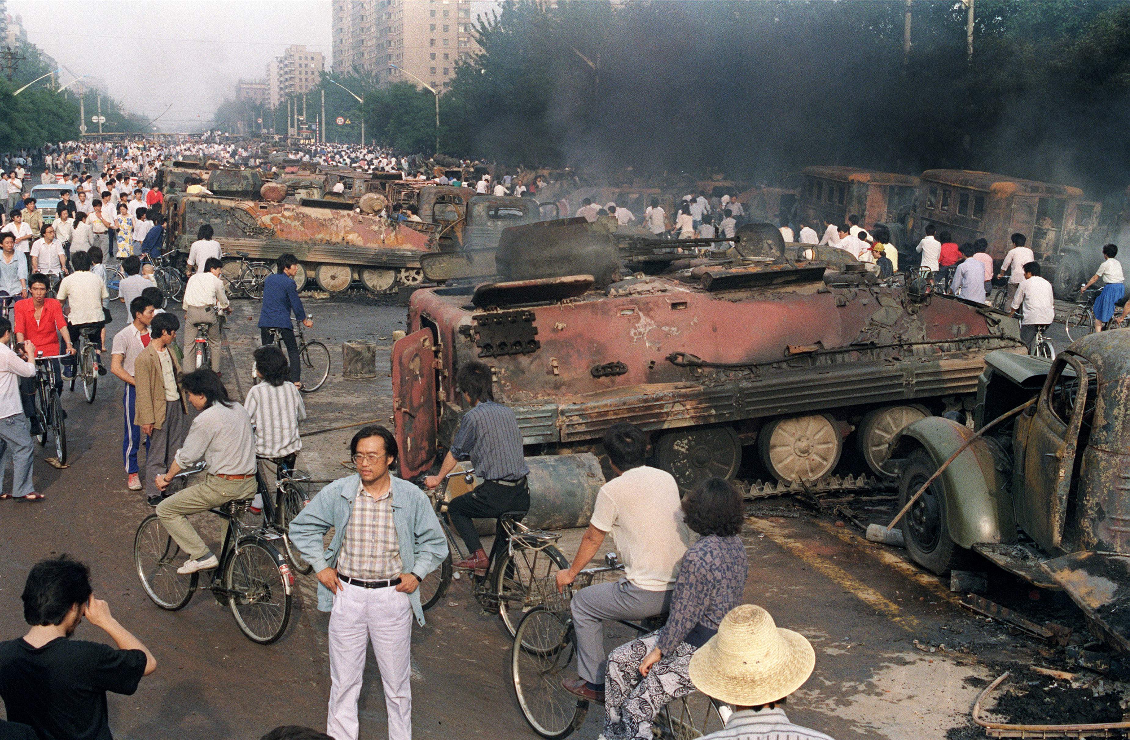 (FILES) In this file photo taken on June 4, 1989, residents gather near the smoking remains of over 20 armoured personnel carriers burnt by demonstrators during clashes with soldiers near Tiananmen Square in Beijing. - After seven weeks of protests by students and workers demanding democratic changes and the end of corruption, soldiers and tanks chased and killed demonstrators and onlookers in the streets leading to the square. But 30 years after the killings of June 4, 1989, the government still keeps a lid on what really happened and how many died on that fateful day. (Photo by Manny CENETA / AFP)