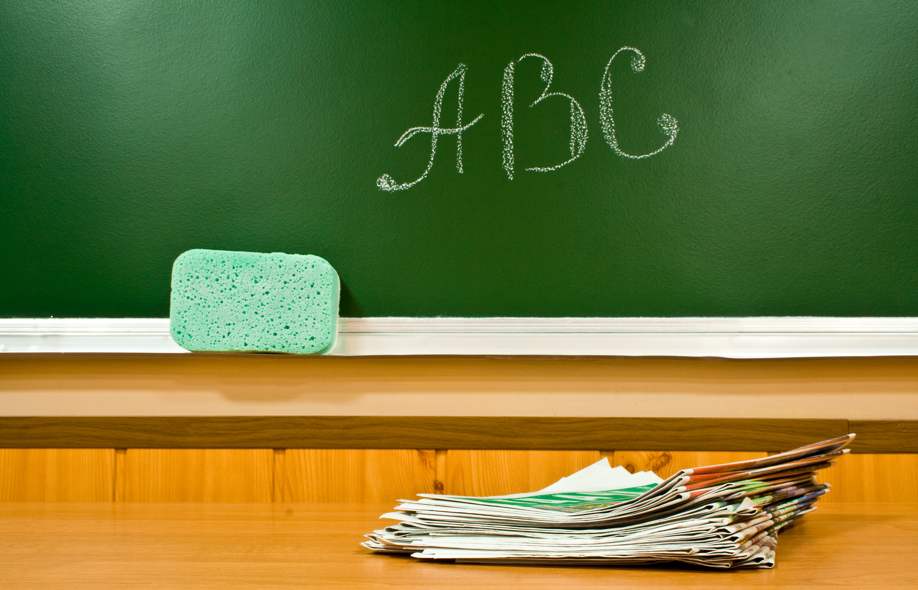 Uso de los periódicos para enseñar y educar en el aula. Cerro de periódicos sobre mesa, con la pizarra al fondo