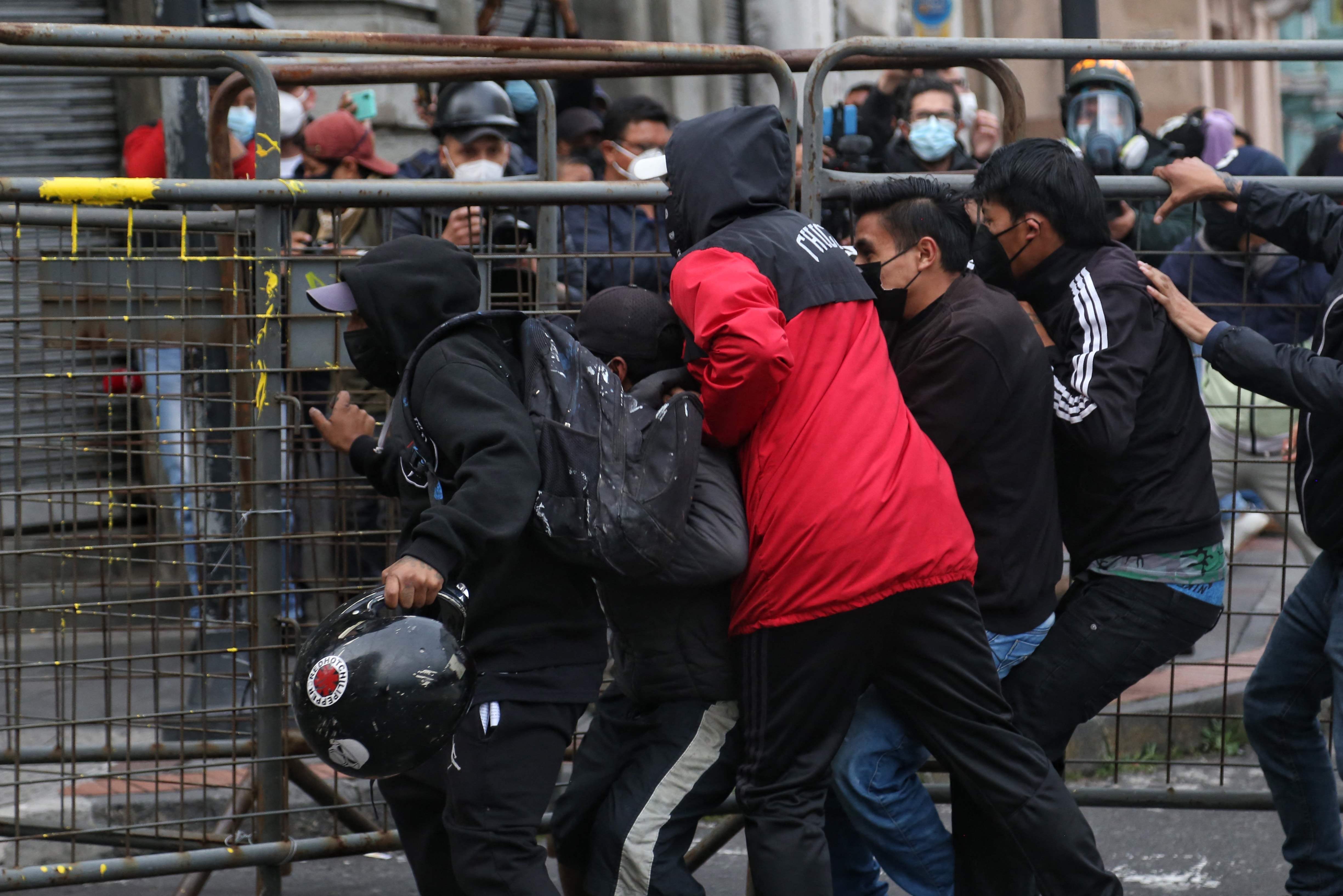 Demonstrators try to tear down a fence during clashes with riot police following a march of members of civil and social organizations, and students, against economic measures imposed by the government, including fuel price hikes, amid a state of emergency, in Quito, on October 26, 2021. - Indigenous people, workers and students will join forces to stage a protest against Ecuador's President Guillermo Lasso, who on October 18 declared a state of emergency in the country grappling with a surge in drug-related violence, and ordered the mobilization of police and military in the streets. (Photo by Cristina Vega RHOR / AFP)