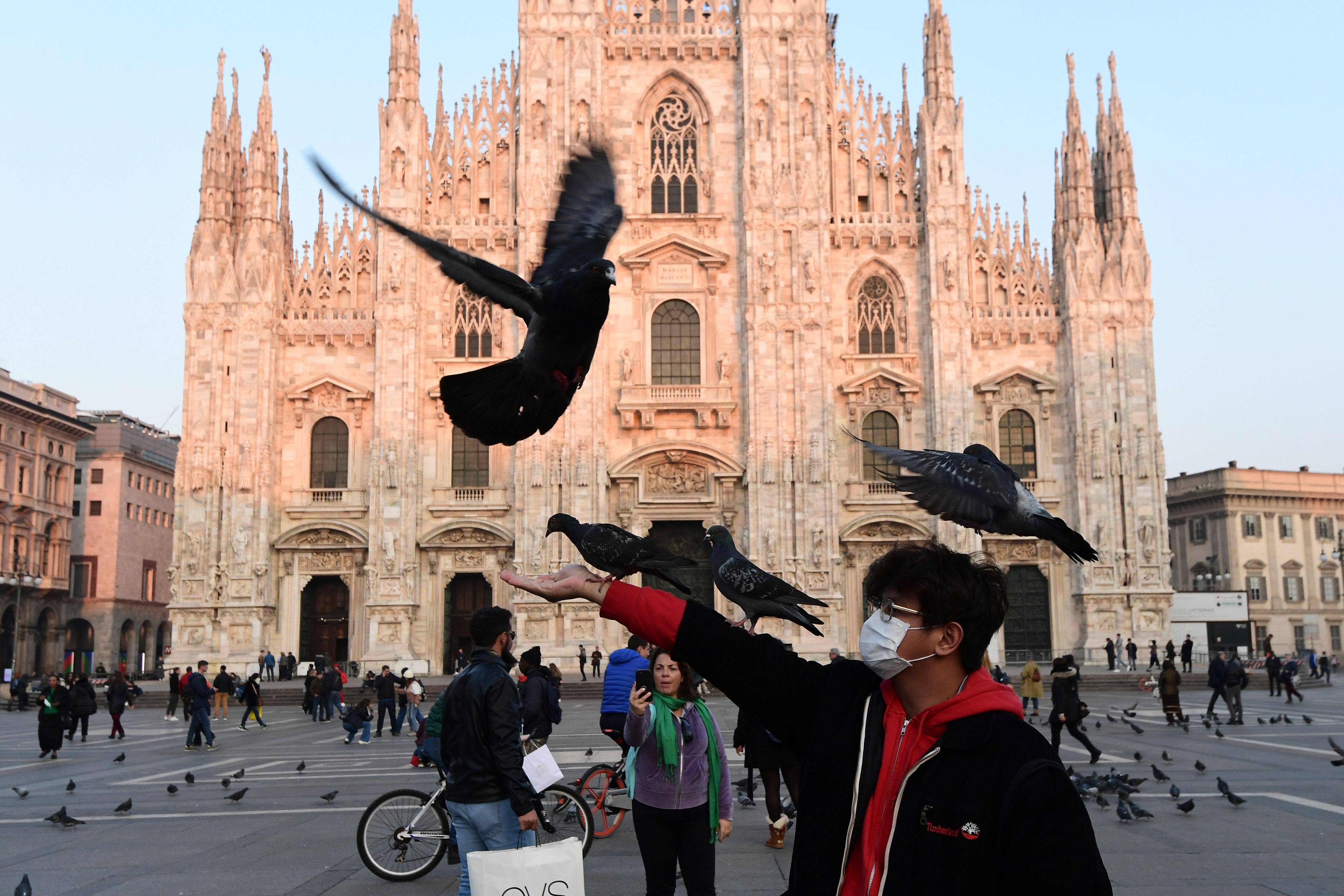 A man wearing a protective facemask plays with pigeons in the Piazza del Duomo in central Milan, on February 24, 2020 following security measures taken in northern Italy against the COVID-19 the novel coronavirus. - Italy reported on February 24, 2020, its fourth death from the new coronavirus, an 84-year old man in the northern Lombardy region, as the number of people contracting the virus continued to mount. (Photo by Miguel MEDINA / AFP)