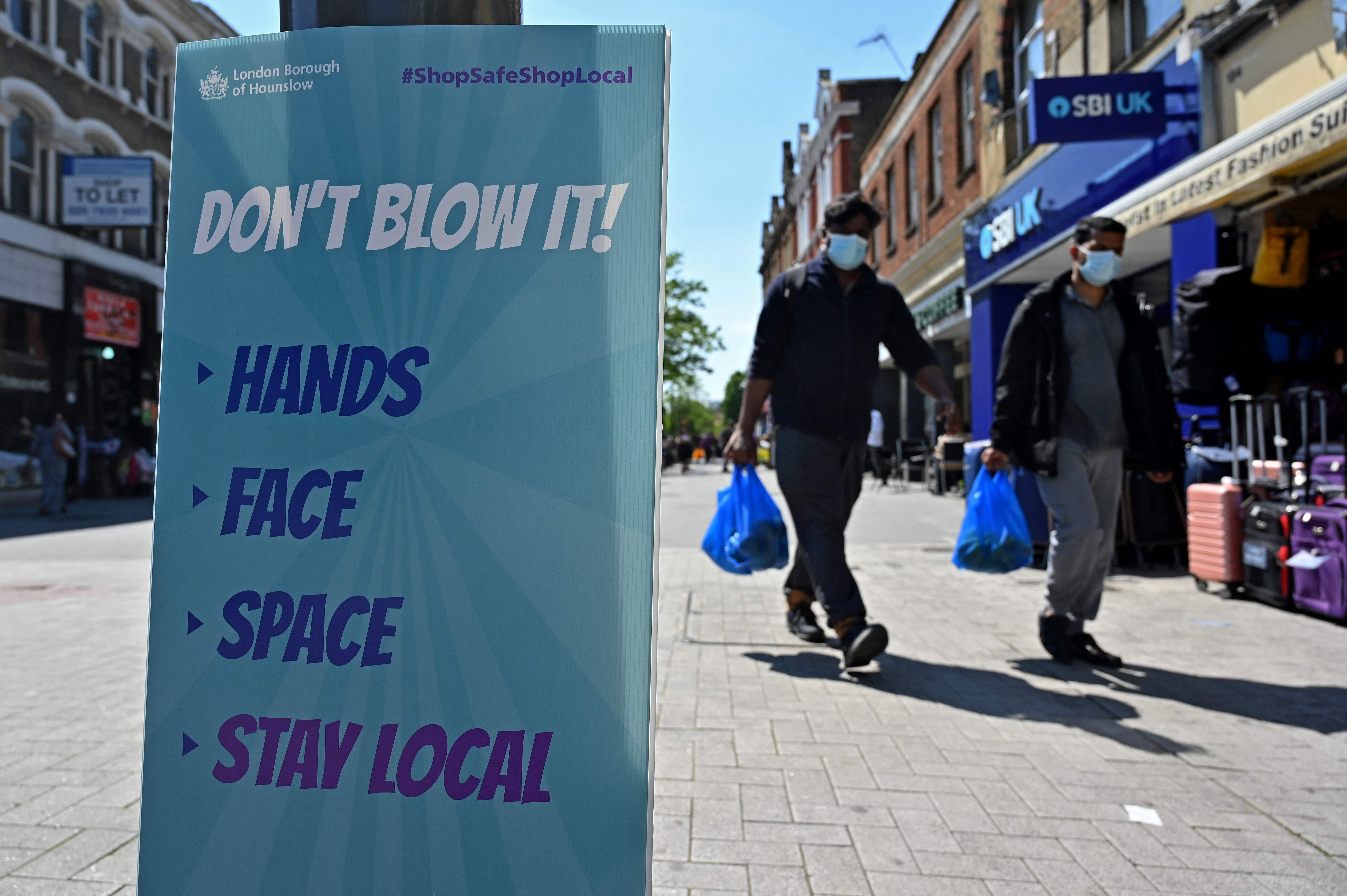 Pedestrians walk past a sign warning members of the public about the spread of Coronavirus as they walk along the street in Hounslow, west London on June 1, 2021. - A rise in cases of the Delta Covid-19 variant, first identified in India, could "pose serious disruption" to Britain's reopening plans, Prime Minister Boris Johnson warned last week. (Photo by JUSTIN TALLIS / AFP)
