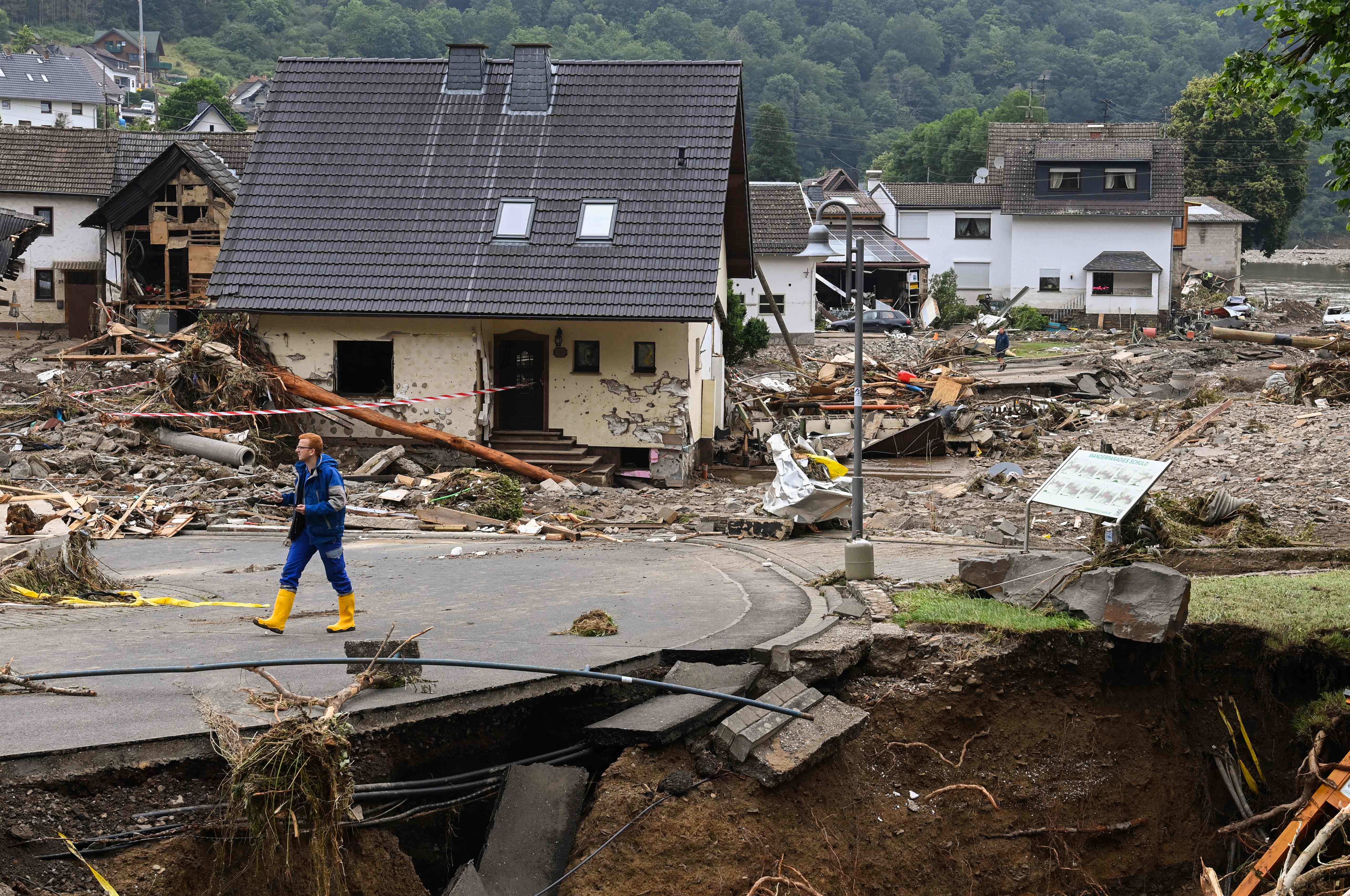 TOPSHOT - A man walk on a partially slipped road amid destroyed houses after the floods caused major damage in Schuld near Bad Neuenahr-Ahrweiler, western Germany, on July 16, 2021. - Devastating floods have torn through entire villages and killed at least 129 people in Europe, most of them in western Germany where stunned emergency services were still combing the wreckage on July 16, 2021. (Photo by CHRISTOF STACHE / AFP)