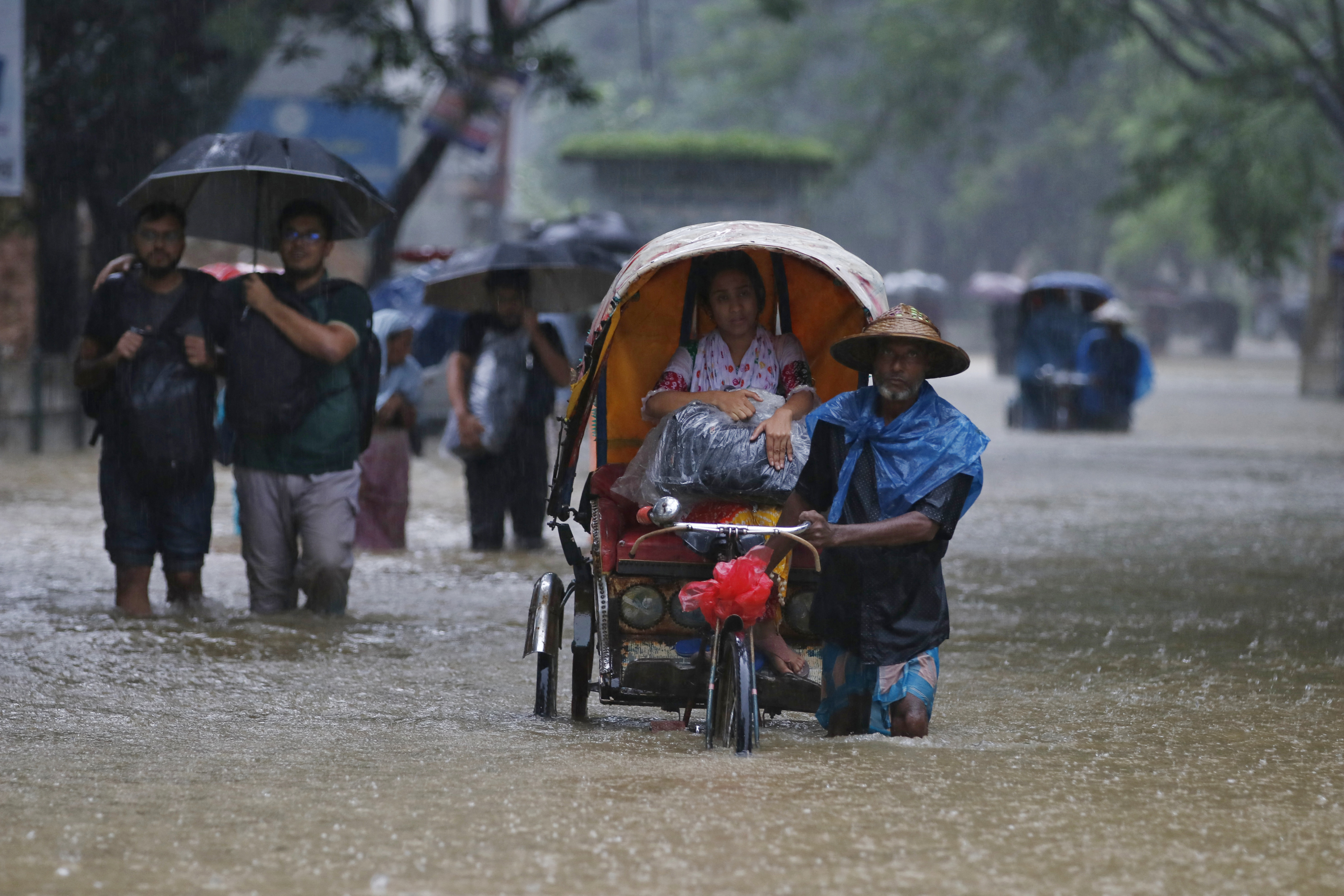 People wade along a road in a flooded area during a monsoon rainfall in Sylhet on June 18, 2022. - Monsoon storms in Bangladesh and India have killed at least 59 people and unleashed devastating floods that left millions of others stranded, officials said on June 18. (Photo by MD Abu Sufian Jewel / AFP)