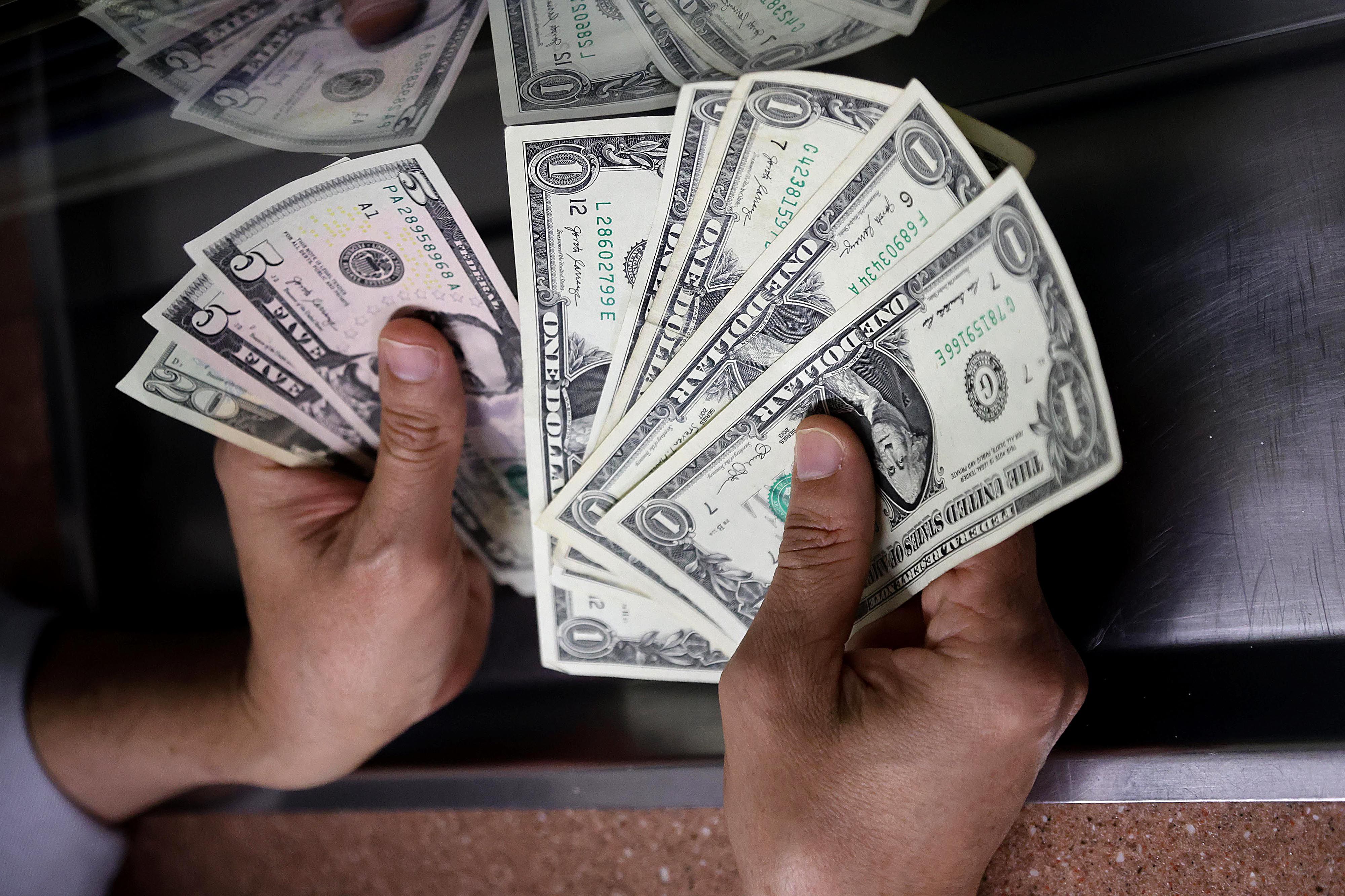 Manos sosteniendo billetes de dólares estadounidenses, ilustrando la caída del tipo de cambio en Costa Rica en febrero de 2025.