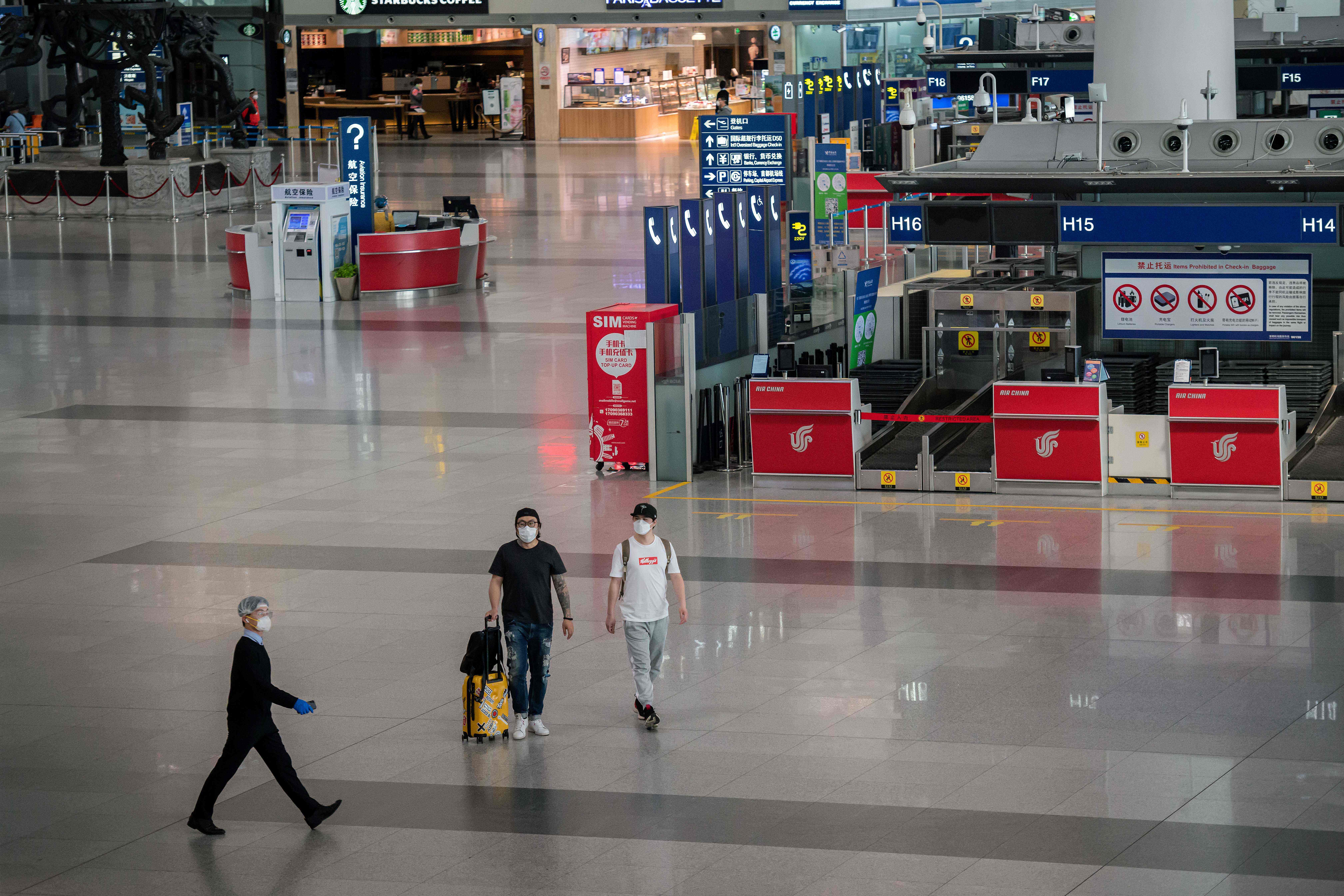 Passangers (C) and an airport staff (L) wearing facemasks amid the concerns over the COVID-19 coronavirus walk in a nearly empty terminal at Beijing Capital International Airport on April 13, 2020. - There were 108 new cases of the coronavirus reported in China, the majority of which were imported cases. According to the National Health Commission, two more people have died, bringing the official toll in mainland China to 3,341. (Photo by NICOLAS ASFOURI / AFP)