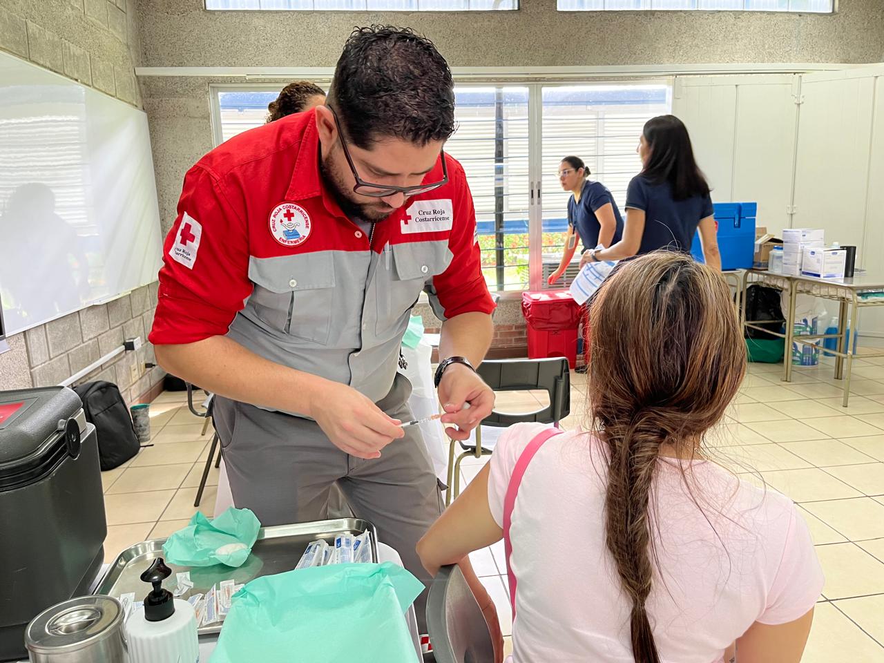 Hombre cruzrojista vacuna a mujer, que está de espaldas.