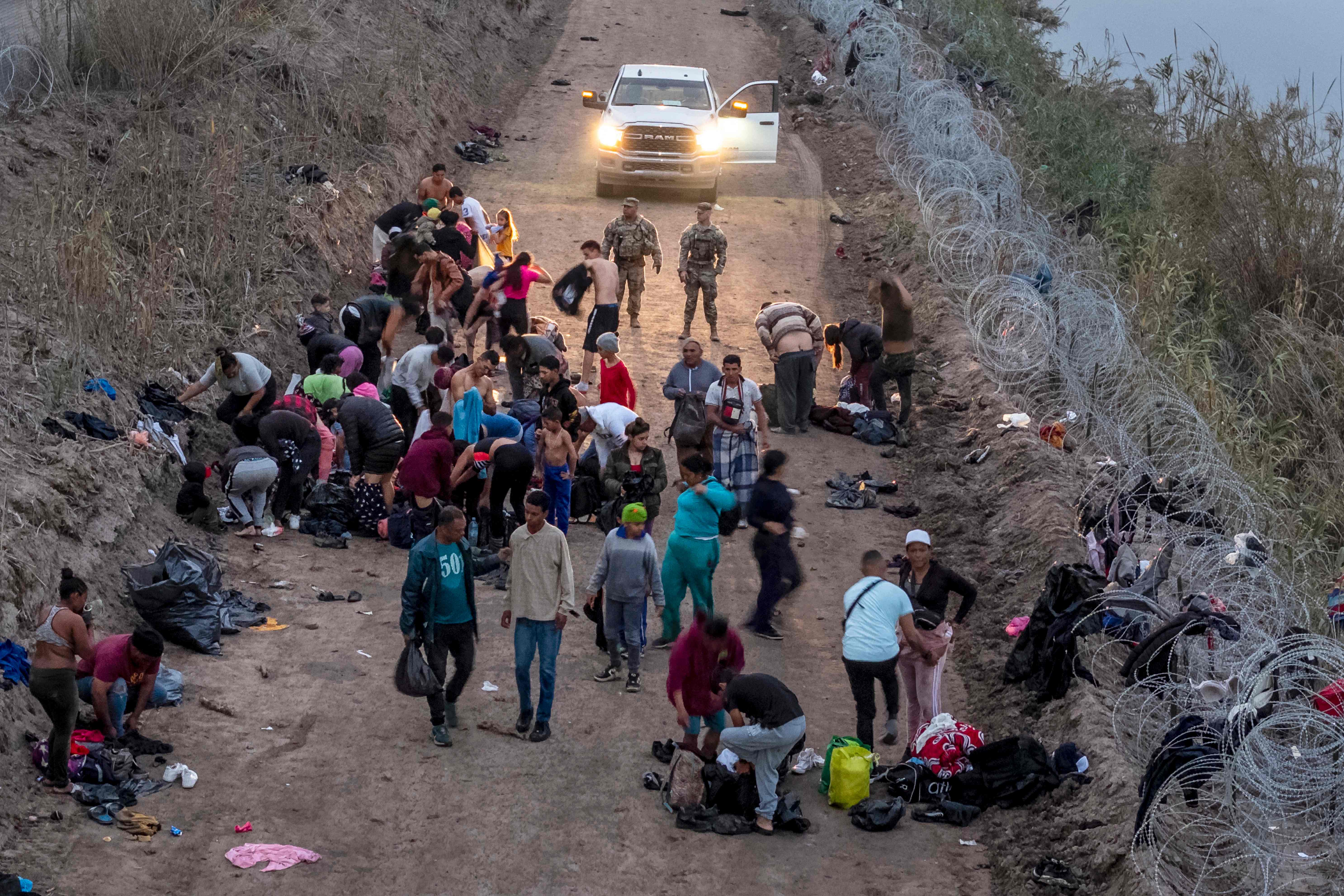 EAGLE PASS, TEXAS - DECEMBER 20: Seen from an aerial view, Texas National Guard troops look on as immigrants change into dry clothes after wading through the Rio Grande from Mexico early on December 20, 2023 in Eagle Pass, Texas. A late-year surge of migrants crossing the U.S. southern border has overwhelmed U.S. immigration officials. John Moore/Getty Images/AFP (Photo by JOHN MOORE / GETTY IMAGES NORTH AMERICA / Getty Images via AFP)