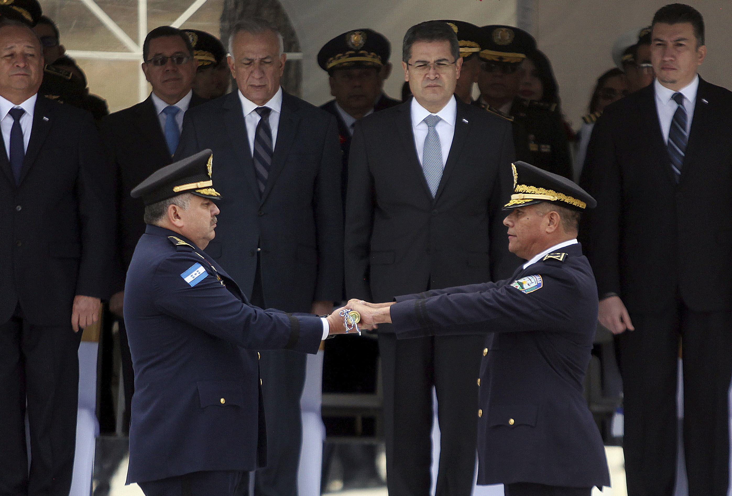 #6393 In this Jan. 15, 2018 photo, Honduran President Juan Orlando Hernandez, behind second from right, watches the change of command exchange ceremony between his new National Police Chief Jose David Aguilar Moran, left, and outgoing Gen. Felix Villanueva in Tegucigalpa, Honduras. A confidential government report obtained by the Associated Press alleges that Aguilar helped a cartel leader pull off the delivery of nearly a ton of cocaine, raising questions about Honduras' much-touted purge of corrupt police and the reliability of the administration of Hernandez, a key U.S. ally in the war on drugs. (AP Photo)