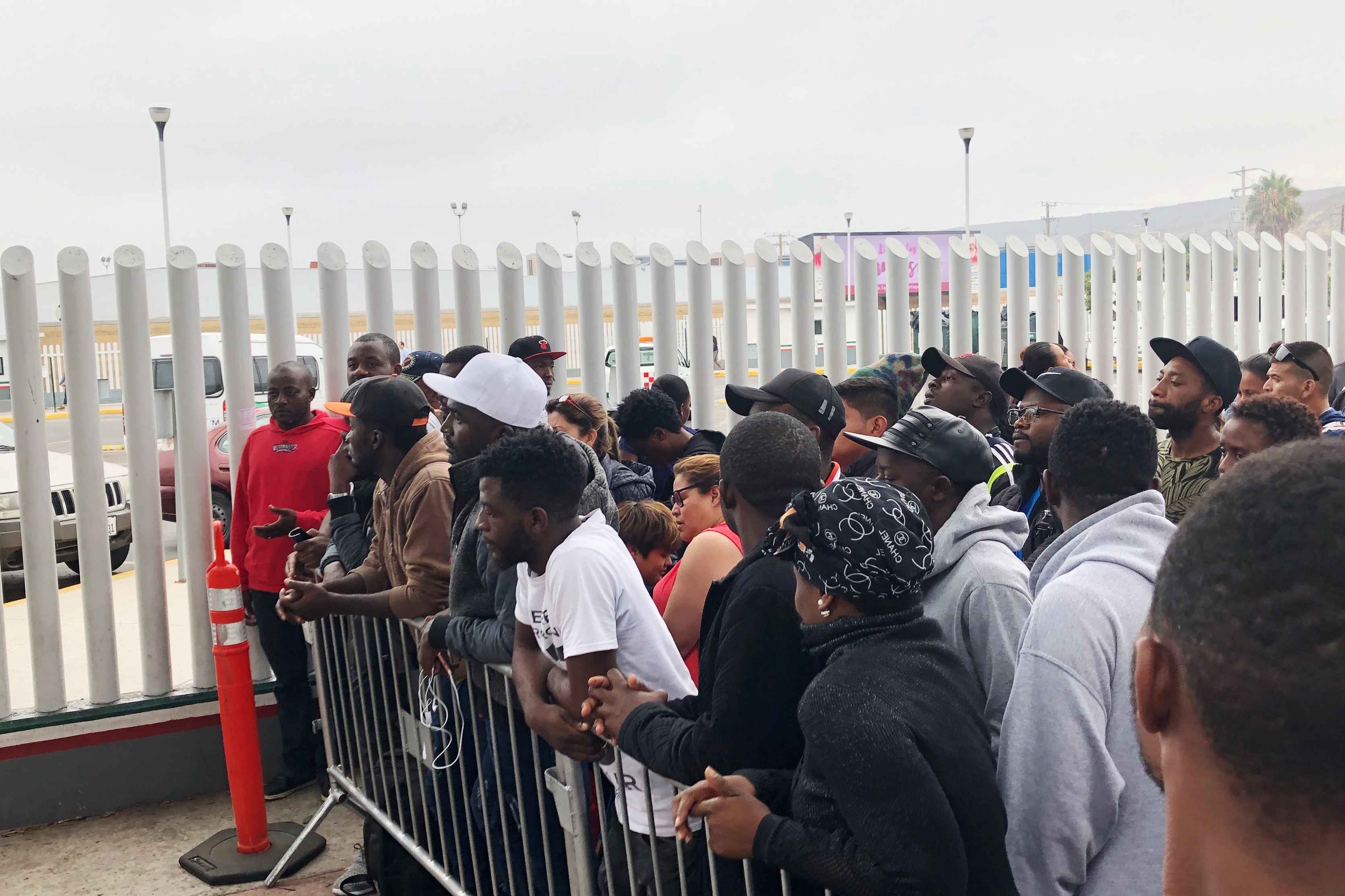 In this Sunday, July 28, 2019, photo, migrants in Tijuana, many from Cameroon, listen to names being called for those who can claim asylum that day in the US. English-speaking Cameroonians fleeing atrocities of their French-speaking government helped push Tijuana’s asylum wait list to 10,000 on Sunday, up from 4,800 just three months earlier. (AP Photo/Elliot Spagat)