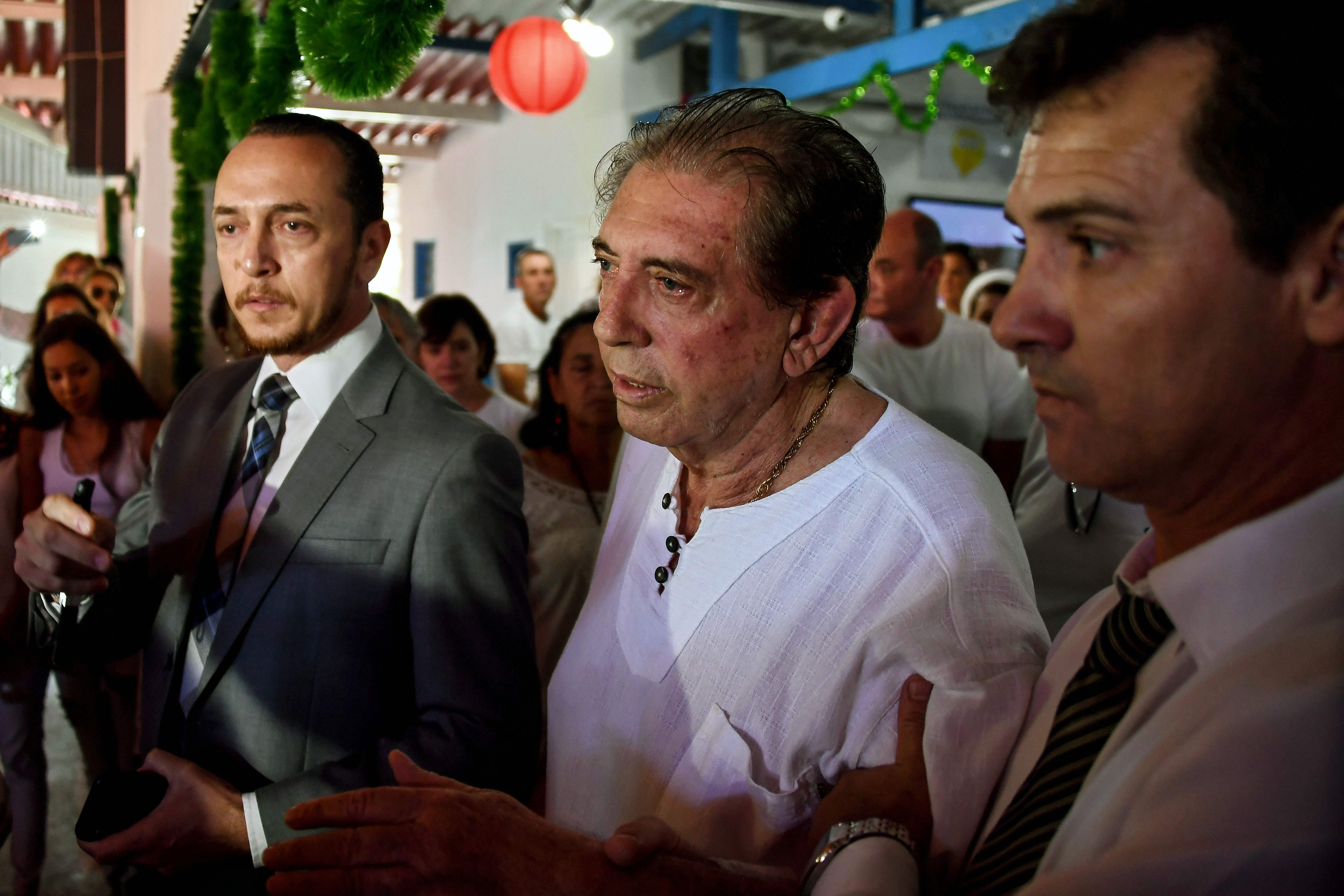 Brazilian "spiritual healer" Joao Teixeira de Faria (C), known as "Joao de Deus" (John of God) is escorted by supporters, upon arrival at his "healing center" Casa de Dom Inacio de Loyola, in Abadiania, 120 km southwest of Brasilia, state of Goias on December 12, 2018. - An internationally famous Brazilian "spiritual healer" accused by hundreds of women of sexual abuse told his followers on Wednesday "I am not guilty" of the allegations stacked against him. Police are starting to investigate complaints lodged by more than 450 women in Brazil following claims by a dozen of his followers aired by Globo TV and the O Globo newspaper last week that he forced them into sex acts under pretext of curing them of ailments. (Photo by EVARISTO SA / AFP)