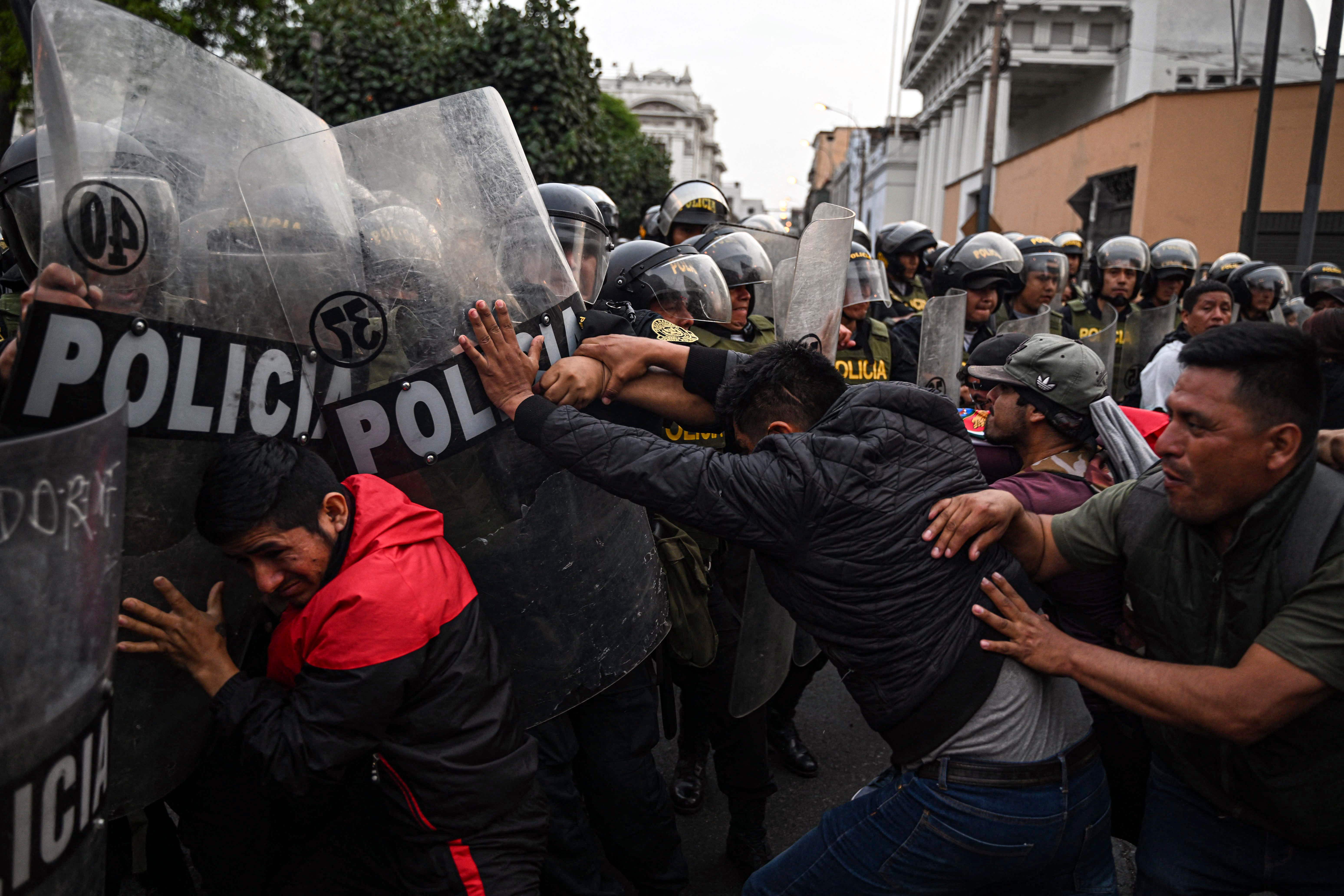 TOPSHOT - People clash with riot police during a demonstration demanding the release of ex-President Pedro Castillo and the closure of the Peruvian Congress, in Lima, on December 8, 2022, a day after Castillo's impeachment. - Castillo was replaced by his deputy on the eve, in a dizzying series of events in the country that has long been prone to political upheaval. Peru has had six presidents in six years in a headspinning political environment where governments topple like dominos, many dogged by corruption scandals in a country with a massive gulf between rich and poor. (Photo by Ernesto BENAVIDES / AFP)