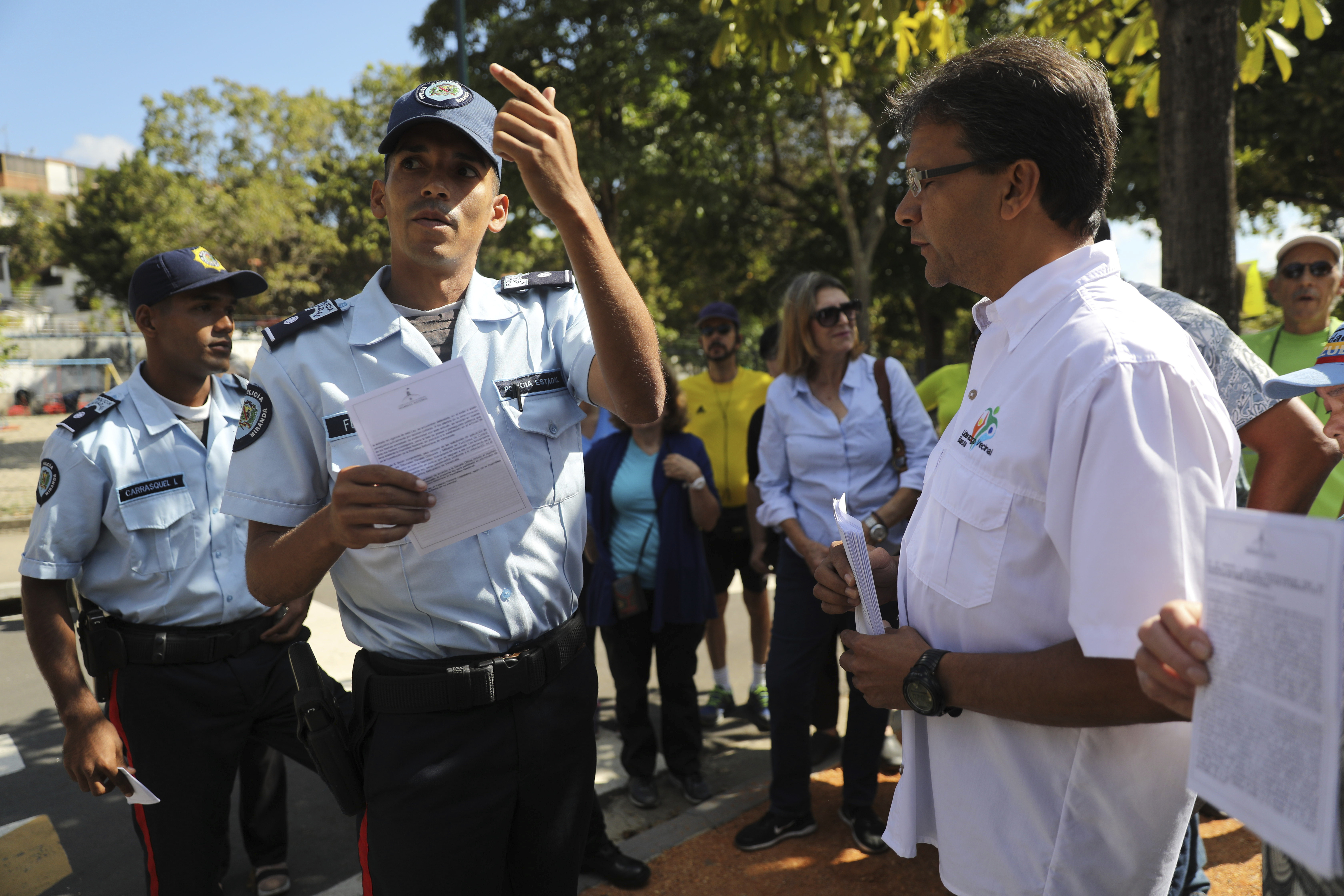 A man from the opposition, right, hands out copies of an amnesty law to members of the military near Ft. Tiuna military base in Caracas, Venezuela, Sunday, Jan. 27, 2019. Opposition National Assembly leader Juan Guaido, who declared himself interim president, said Friday that he would release the text of an existing amnesty law that would pardon members of the military who cooperate in restoring democracy and asked Venezuelans to share it with officers they know. (AP Photo/Rodrigo Abd)