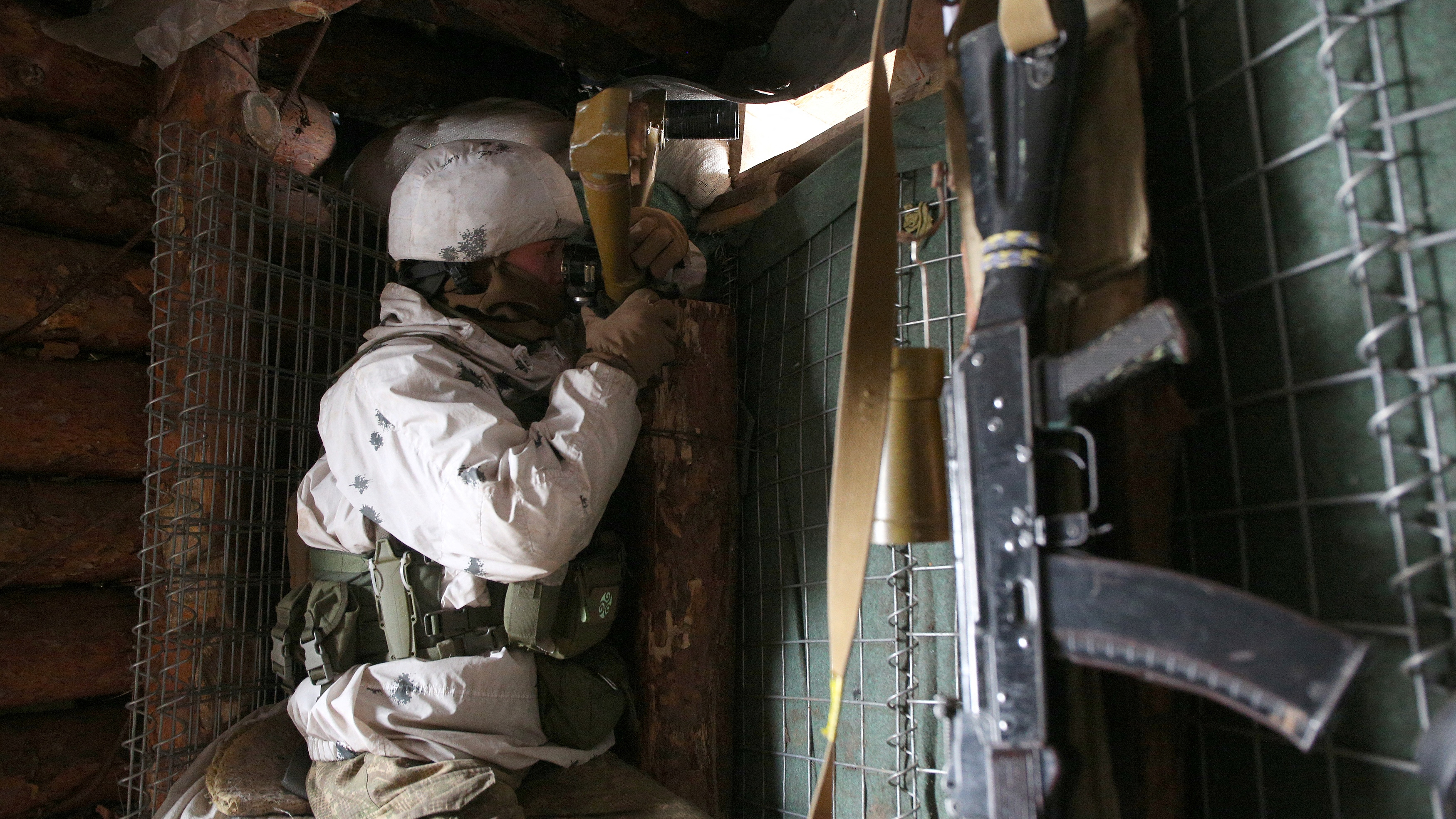 An Ukrainian Military Forces serviceman, watches through spyglass in a dugout on the frontline with Russia-backed separatists near Gorlivka, Donetsk region on January 23, 2022. (Photo by Anatolii STEPANOV / AFP)