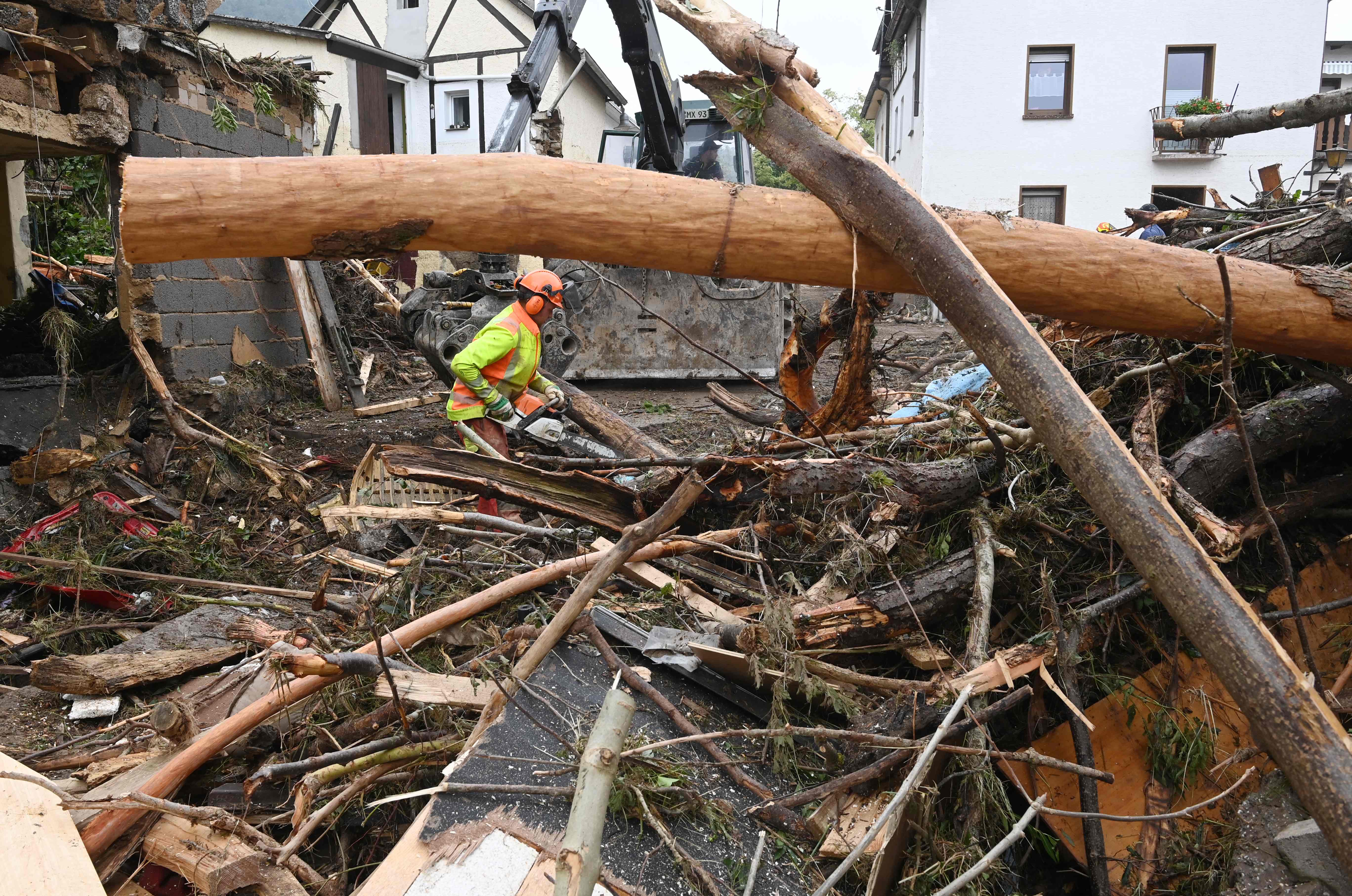 TOPSHOT - A worker cuts and removes uprooted trees fallen among debris amid destroyed houses after the floods caused major damage in Schuld near Bad Neuenahr-Ahrweiler, western Germany, on July 17, 2021. - Devastating floods in Germany and other parts of western Europe have been described as a "catastrophe", a "war zone" and "unprecedented", with more than 150 people dead and the toll still climbing on July 17, 2021 (Photo by CHRISTOF STACHE / AFP)