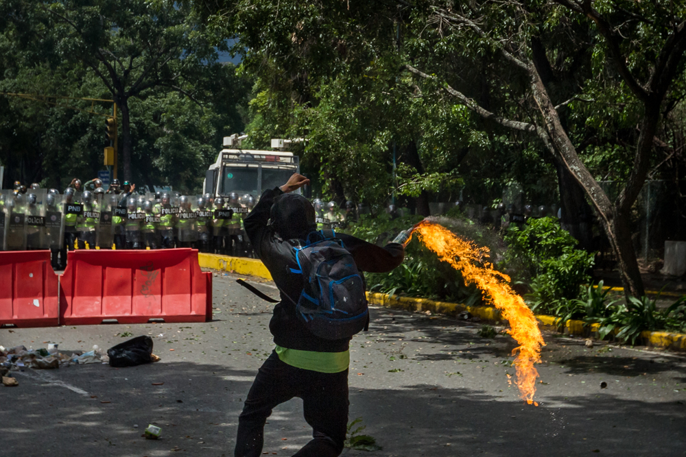 Un estudiante lanza un coctel molotov a miembros de la Policía Nacional Bolivariana (PNB) en la Universidad Central de Venezuela (UCV), este jueves en Caracas. Las autoridades bloquearon el paso de los manifestantes hacia el Tribunal Electoral. | EFE
