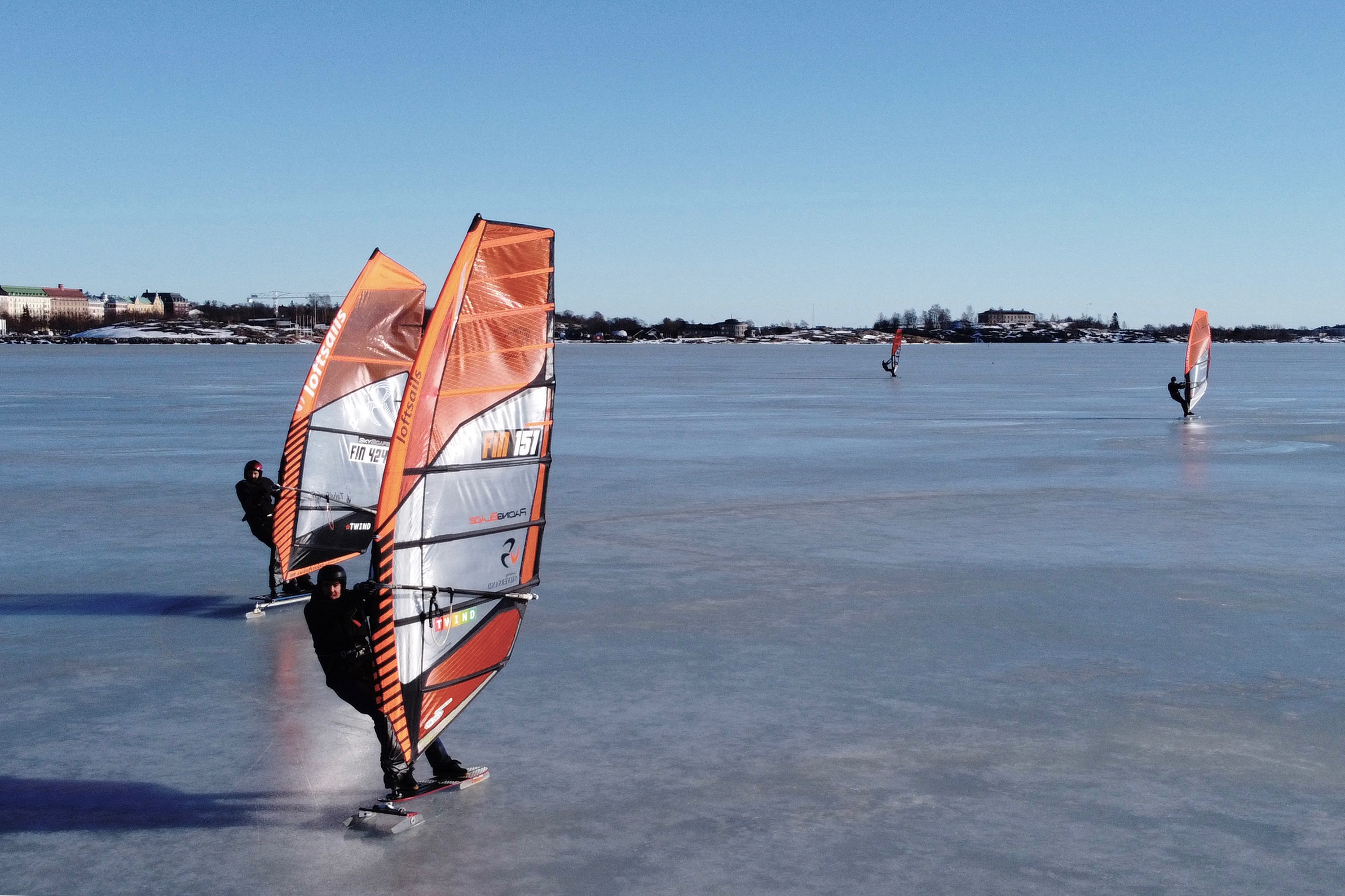 An aerial photo taken on February 28, 2021 shows ice surfers skating across the frozen Baltic Sea off the coast of Helsinki. - What to do if you are a windsurfing enthusiast in a country where the sea freezes over for months of the year? For a group of Finns, the answer is to kit out sailboards with skates and take to the ice, reaching speeds of up to 100km/h (62mph) in a burgeoning sport that can only be practised in a handful of places around the world. (Photo by Sam KINGSLEY / AFP) / TO GO WITH AFP STORY