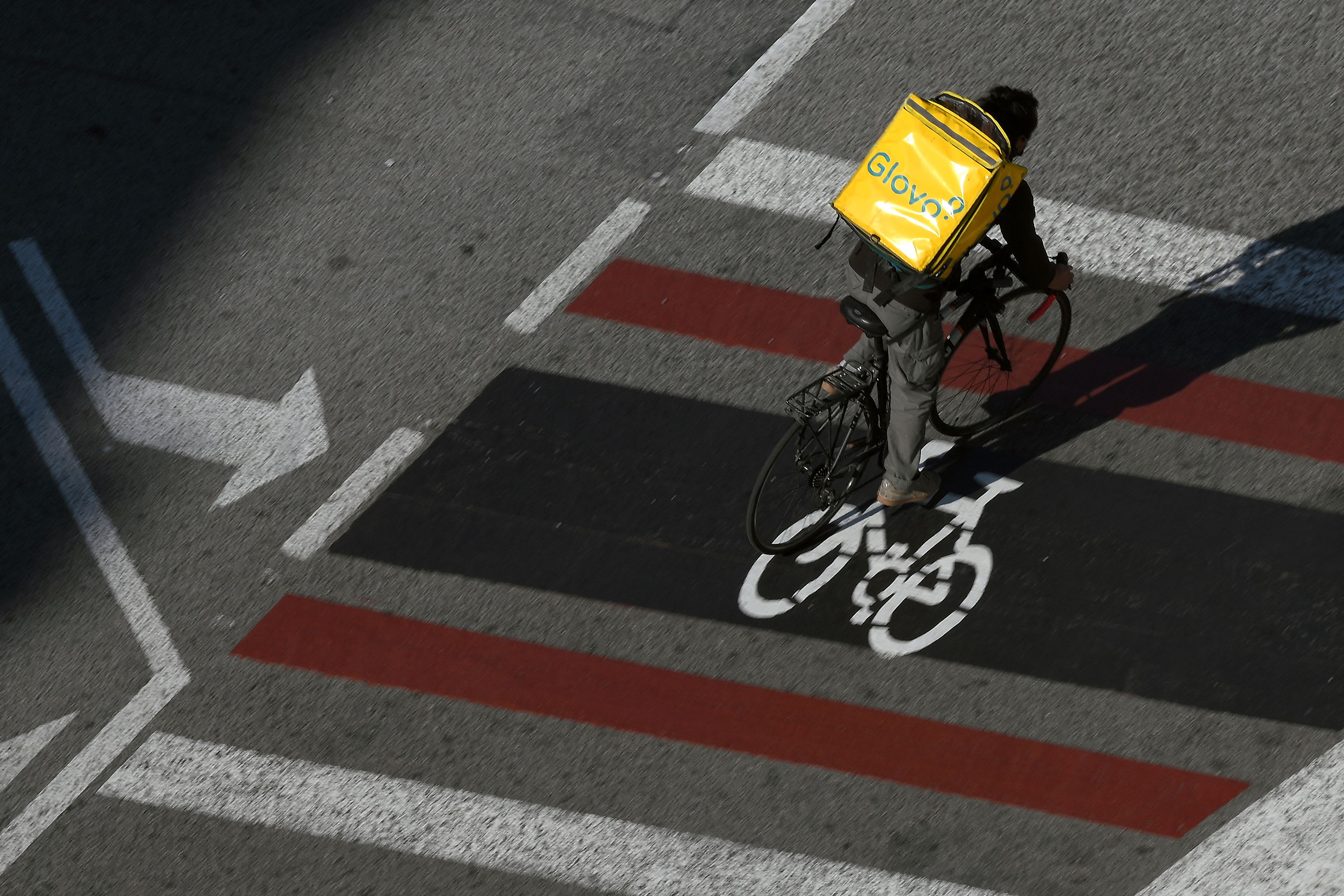 (FILES) In this file photo taken on February 4, 2021 a Glovo delivery worker rides through a street in Barcelona. - Spain's government has inked a deal with unions which will see riders working for delivery firms like Deliveroo and UberEats legally recognised as salaried staff, the labour minister said on March 11, 2021. (Photo by LLUIS GENE / AFP)