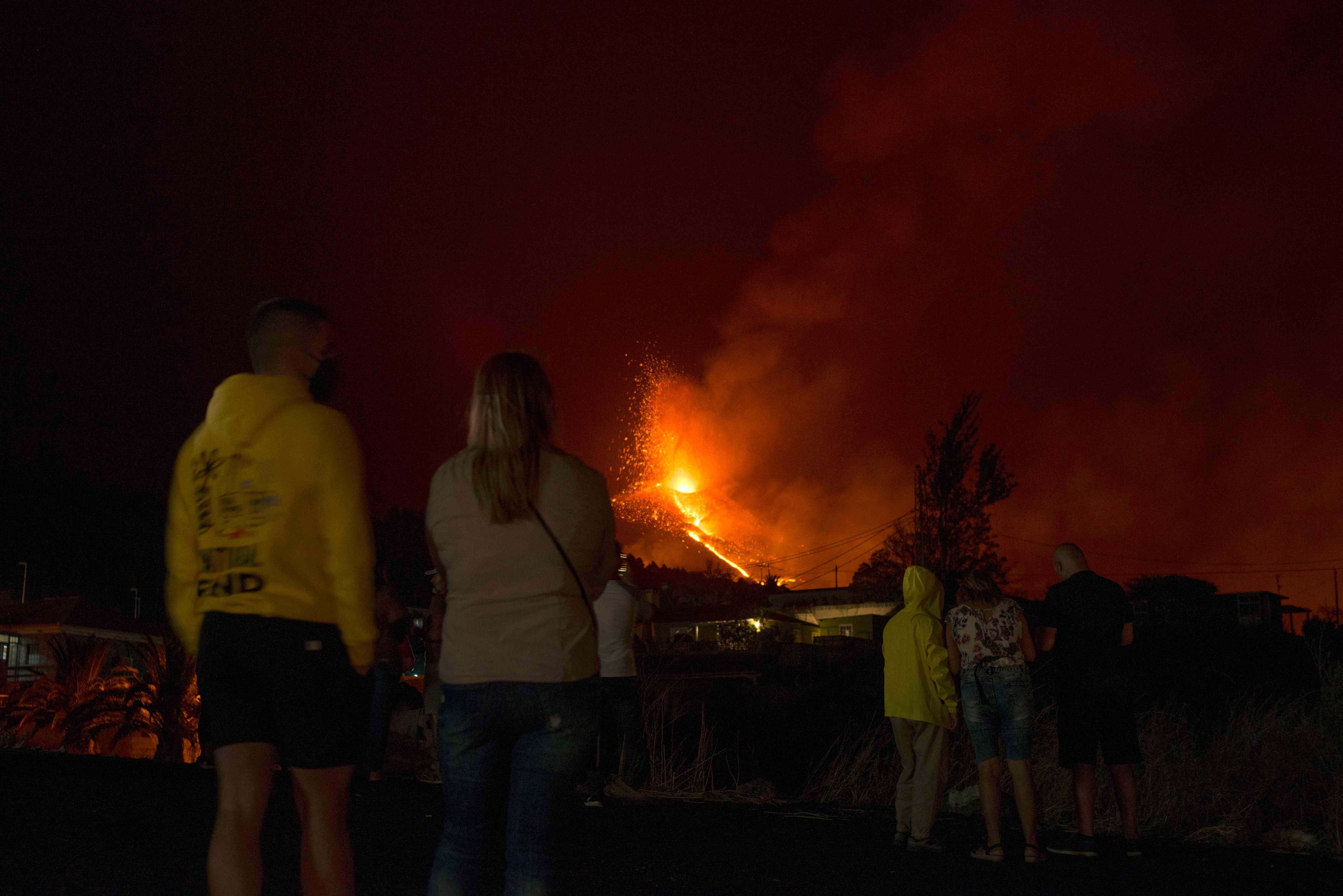 TOPSHOT - People observe the Cumbre Vieja volcano spewing lava, ash and smoke from El Paso, in the Canary Island of La Palma late on October 2, 2021. - A new flow of highly liquid lava emerged from the volcano erupting in Spain's Canary islands on October 1, authorities said, as a huge magma shelf continues to build on the Atlantic ocean. (Photo by JORGE GUERRERO / AFP)