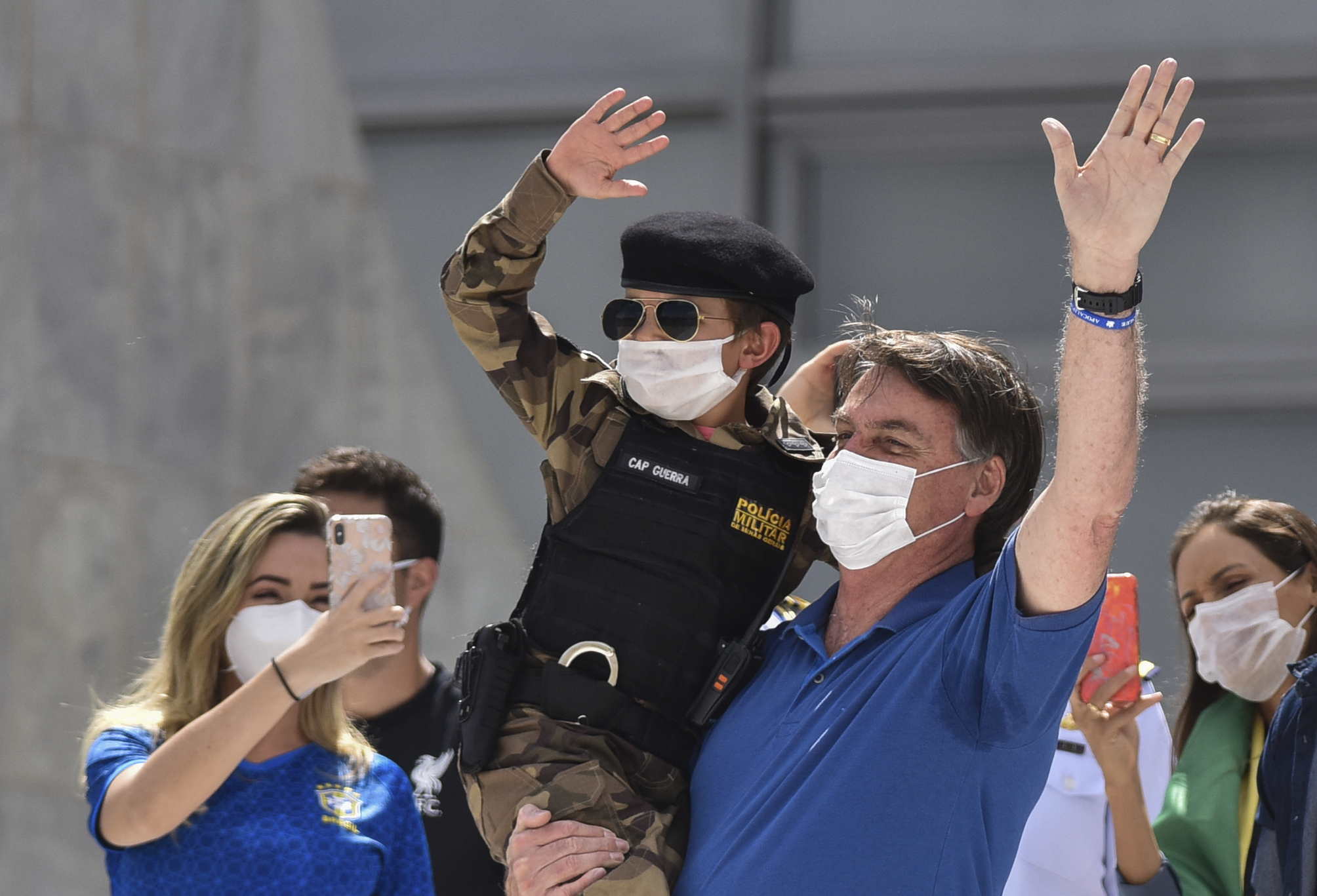 Brazil's President Jair Bolsonaro, wearing a mask against the spread of the new coronavirus, carries a child dressed in military policeman's uniform during a protest against the Supreme Court and Brazil's National Congress, to back his open-the-economy drive amid the pandemic, in Brasilia, Brazil, Sunday, May 17, 2020. Bolsonaro greeted hundreds of supporters who gathered at the presidential residence to back his open-the-economy drive even as the COVID-19 pandemic sweeps across the country. (AP Photo/Andre Borges)