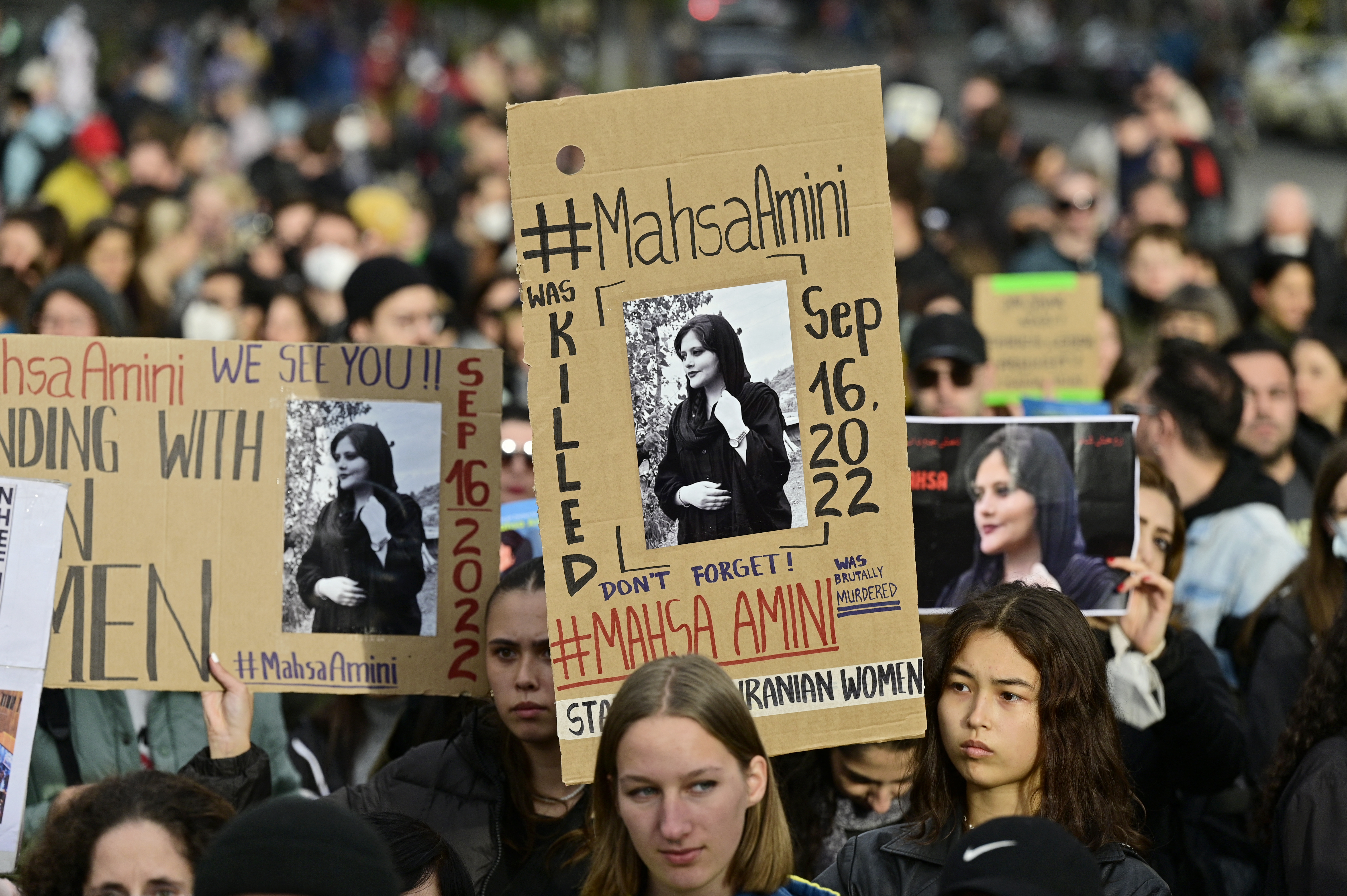 Demonstrators hold up placards with images of Kurdish Iranian woman Mahsa Amini who died while in the custody of Iran's morality police, during a demonstration in support of women and the Iranian protesters, on September 28, 2022 near Berlin's landmark Brandenburg Gate. - Mahsa Amini, 22, has died in September after her arrest in Tehran by the feared morality police for allegedly breaching Iran's strict rules on hijab headscarves and modest clothing for women. She was declared dead on September 16, 2022 by state television after having spent three days in a coma. (Photo by John MACDOUGALL / AFP)