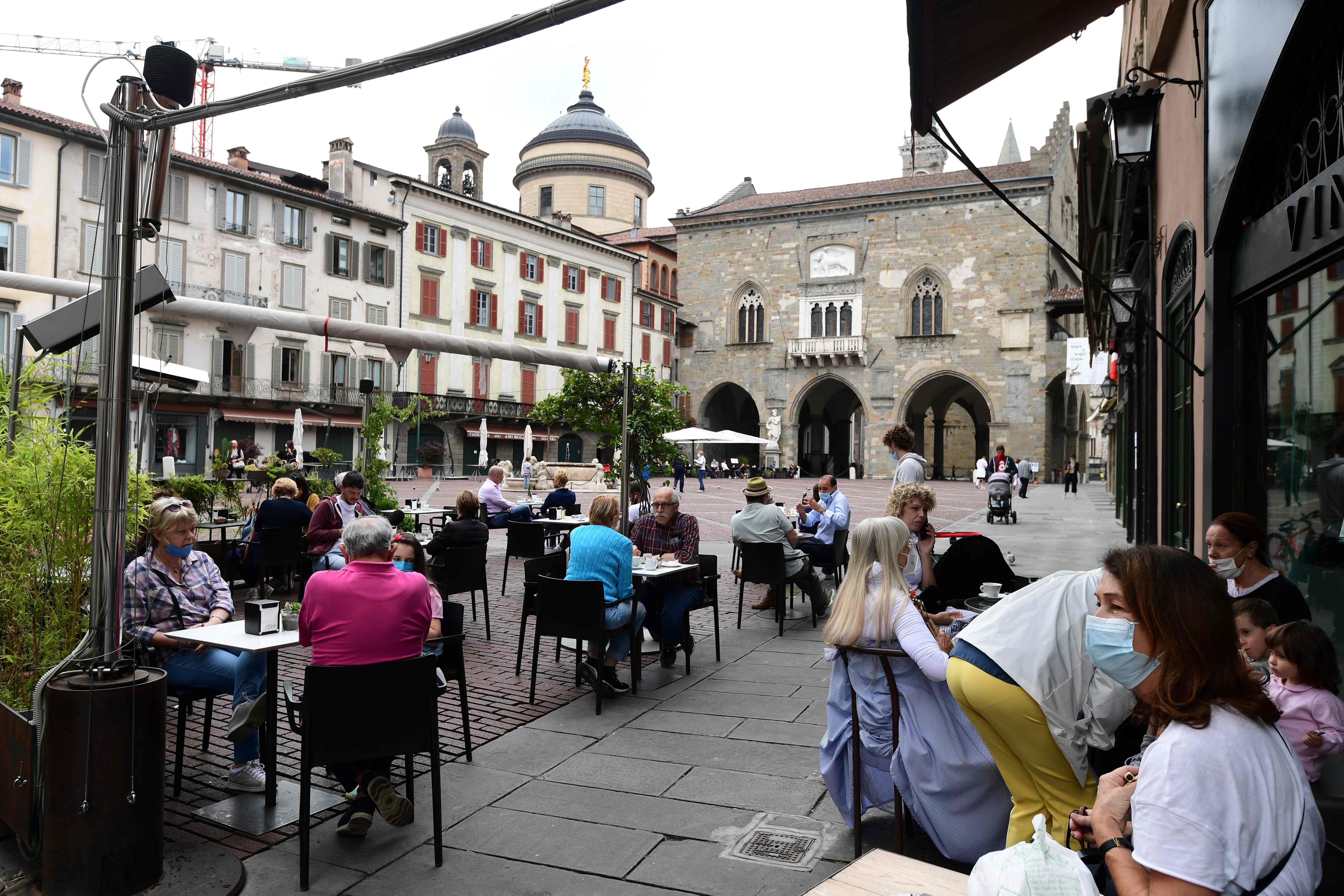 (FILES) In this file photo taken on June 10, 2020 People sit at a cafe's terrace on the Piazza Vecchia in the upper city of Bergamo on June 10, 2020, as Italy eases lockdown measures taken to curb the spread of the COVID-19 disease, caused by the novel coronavirus. - Bergamo, which was hit hard by the coronavirus epidemic, is a martyred city that is now trying to relearn how to live, especially with its football team which resumes its historic season playing in the Serie A championship on June 21. (Photo by Miguel MEDINA / AFP)