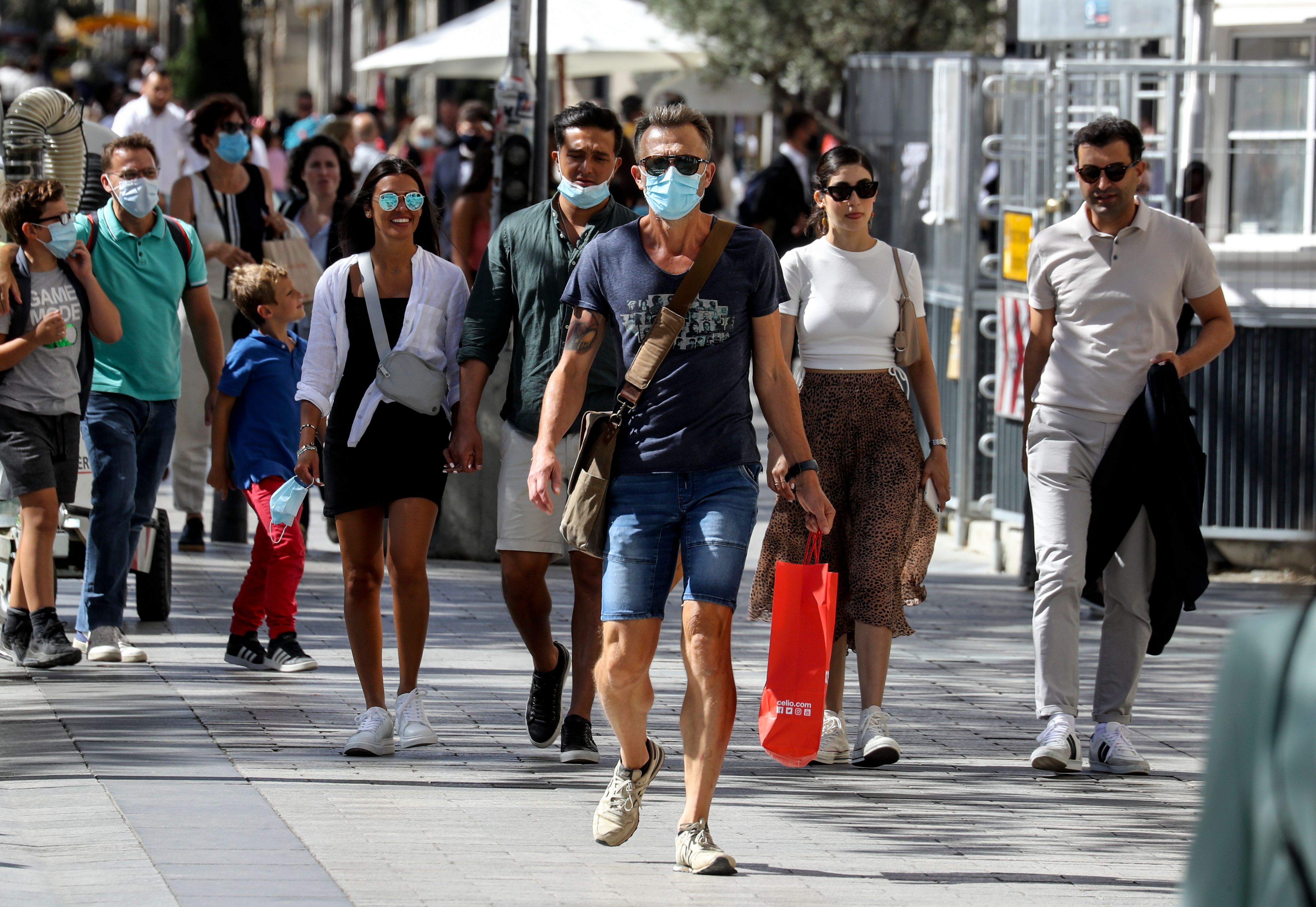 People wearing face masks walk on the Champs Elysees Avenue in Paris, on August 27, 2020. - France's prime minister announced on August 27, 2020, that face masks become compulsory throughout Paris and inner suburbs as he detailed a national trend of expanding coronavirus infections. (Photo by Ludovic MARIN / AFP)