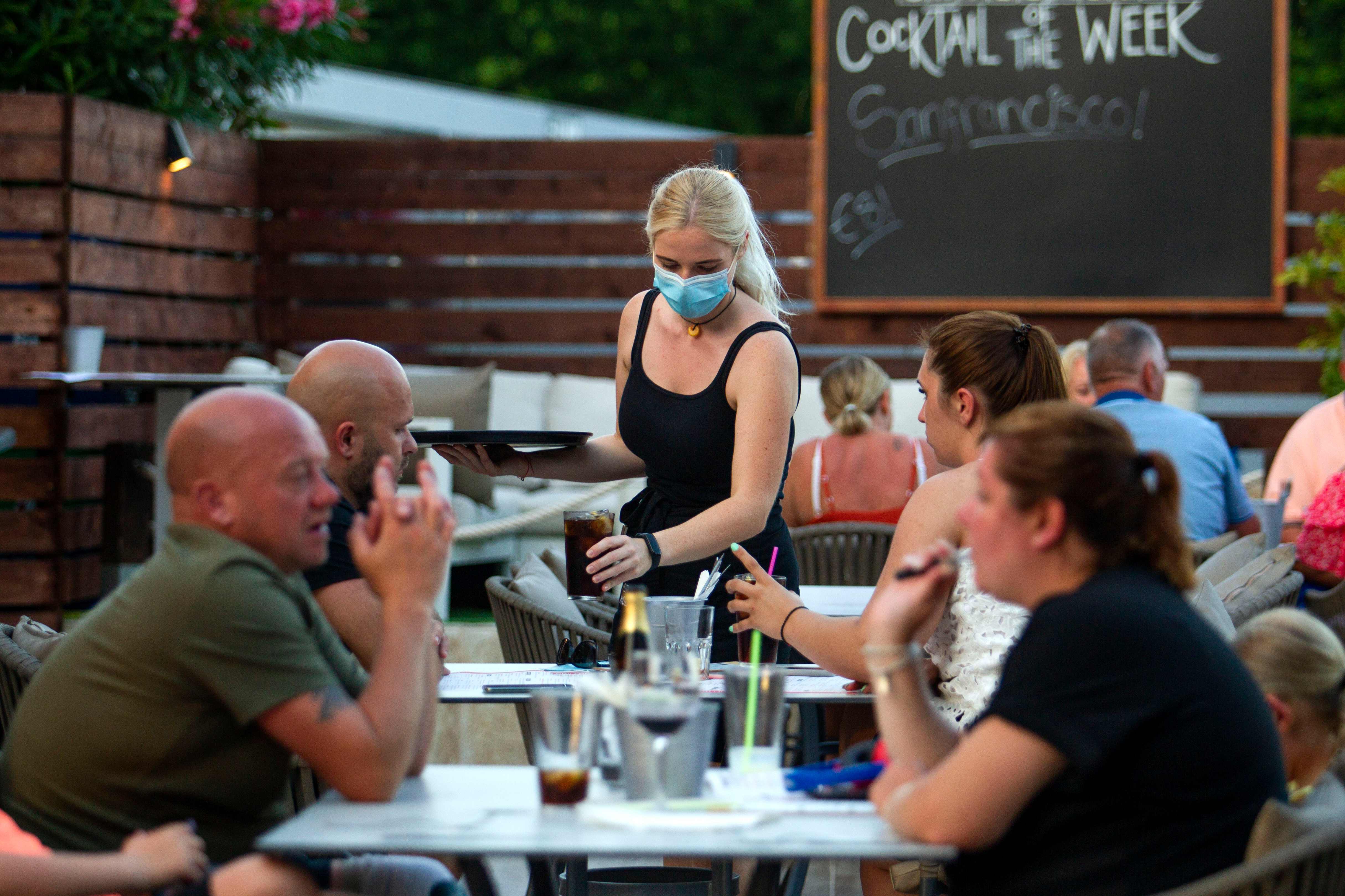 A waitress serves tourists at a restaurant in Palmanova on the Island of Mallorca on July 27, 2020. - Tour operator TUI has cancelled all British holidays to mainland Spain from today until August 9, after the UK government's decision to require travellers returning from the country to quarantine. (Photo by JAIME REINA / AFP)