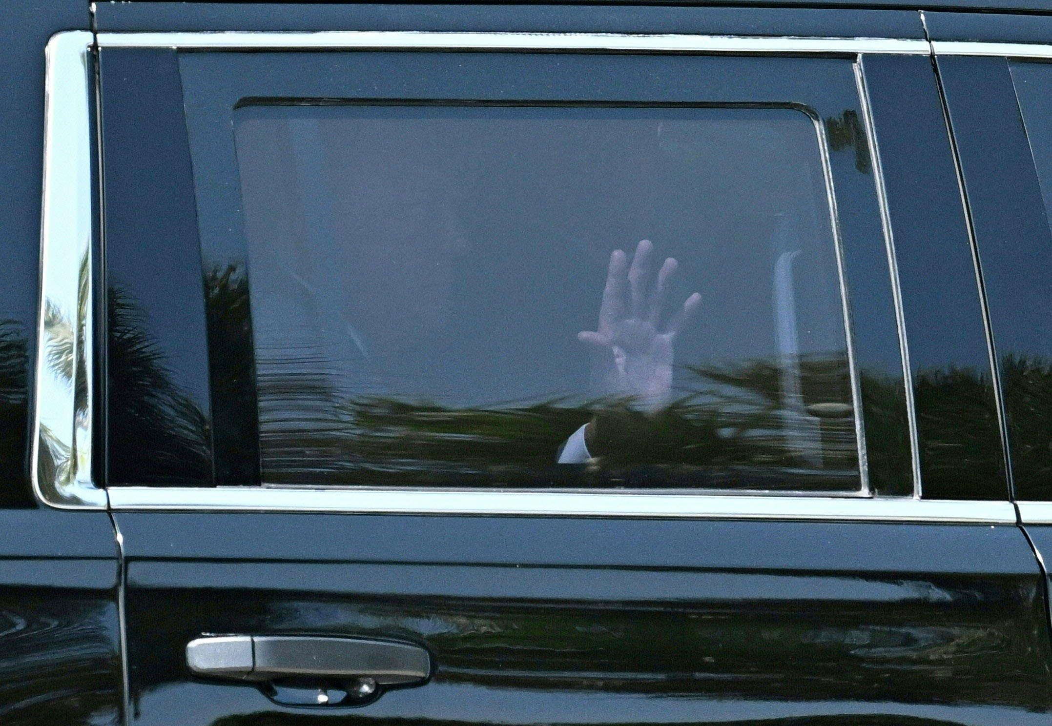 US former President Donald Trump waves as he rides in the back of an SUV as his motorcade arrives at Palm Beach International Airport in West Palm Beach, Florida, on April 3, 2023. - Donald Trump left his Florida home Monday bound for New York where he will surrender to criminal charges, taking the United States into uncharted and potentially volatile territory. (Photo by CHANDAN KHANNA / AFP)