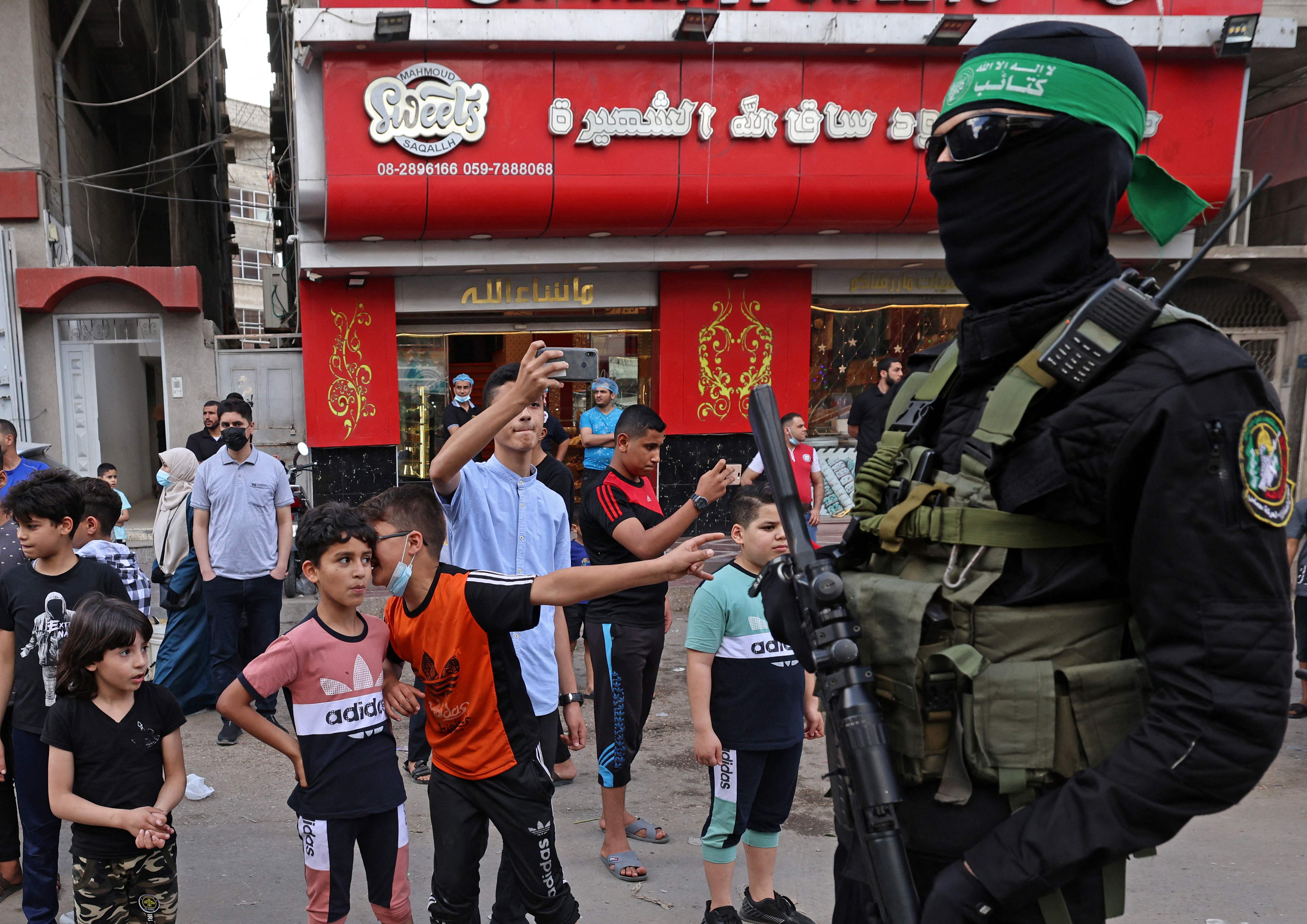 Palestinian boys look at members of Al-Qassam brigades, the armed wing of Palestinian Hamas group, marching in Gaza City on May 22, 2021, in commemoration of Senior Hamas Commander Bassem Issa who was killed along others in Israeli airstrikes. (Photo by Emmanuel DUNAND / AFP)