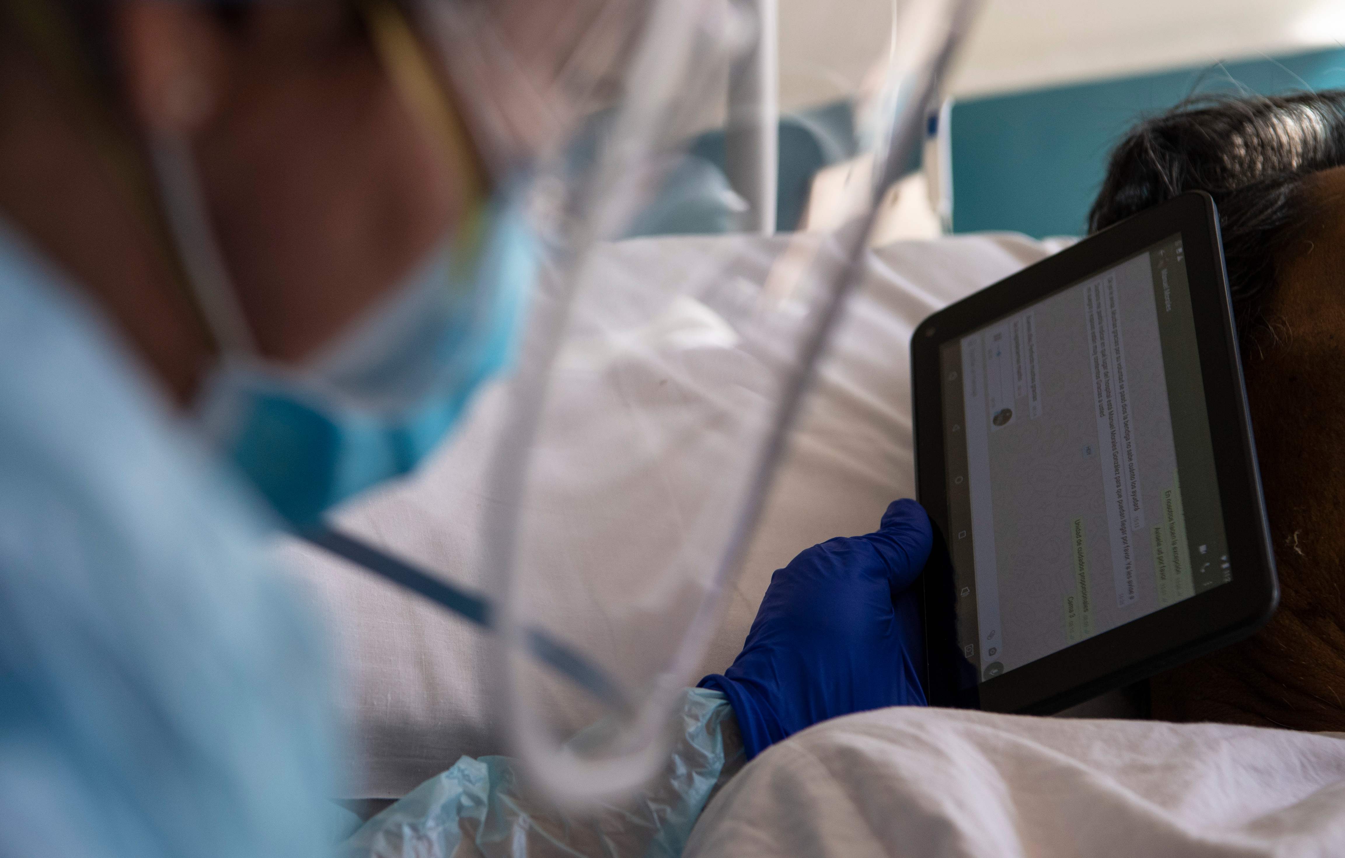 Doctor Moyra Lopez holds an iPad for a terminal patient to listen to a farewell message from his relatives, at the so-called 'humanized farewell' room at the Barros Luco Hospital, in Santiago, July 22, 2020. - As the fatality rate in coronavirus-hit Chile is on a halt, the humanized farewell room first intended only for Covid-19 cases, is now used for all terminal patients. (Photo by MARTIN BERNETTI / AFP)