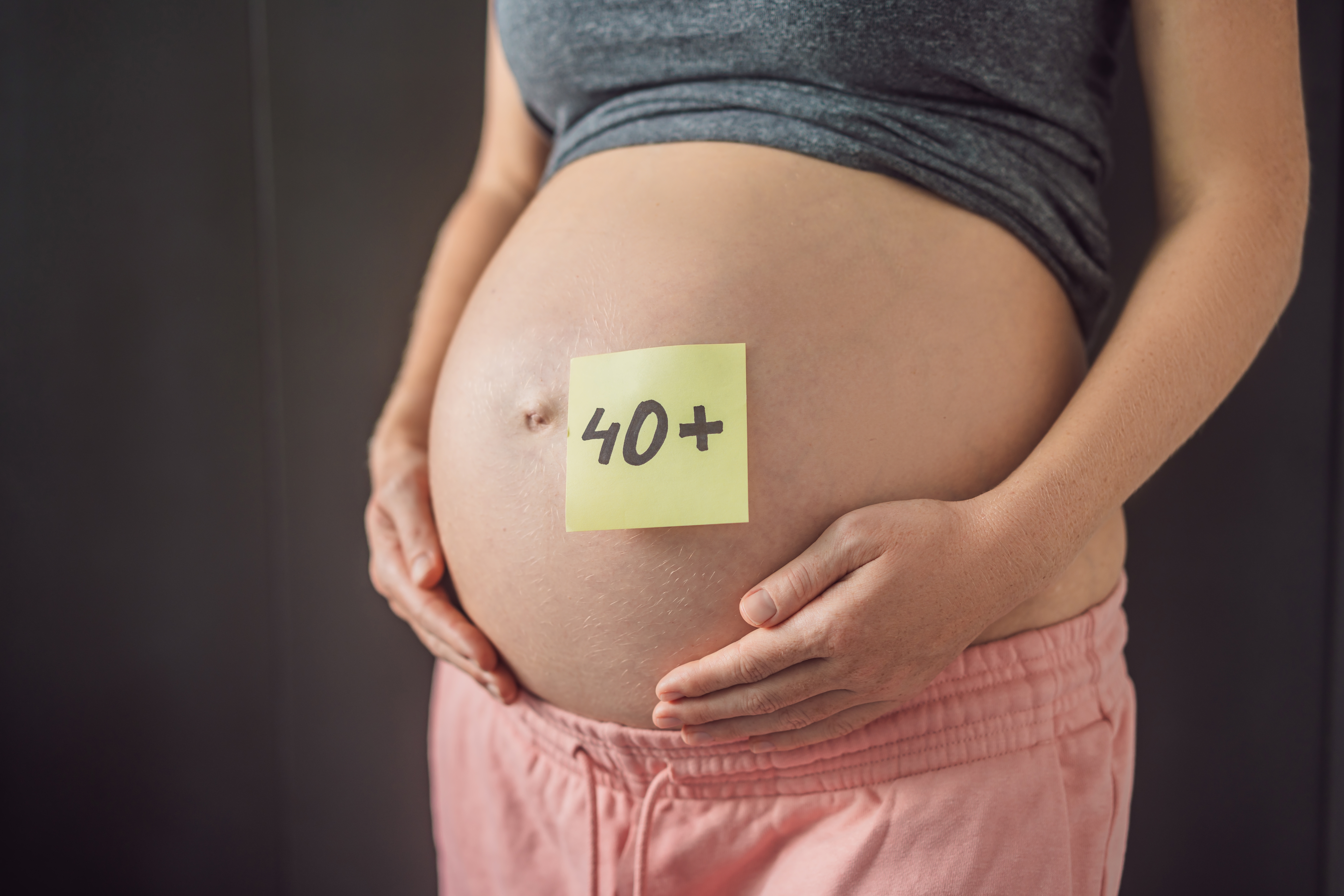 Una mujer embarazada, en su vientre a un papel con la frase 40+