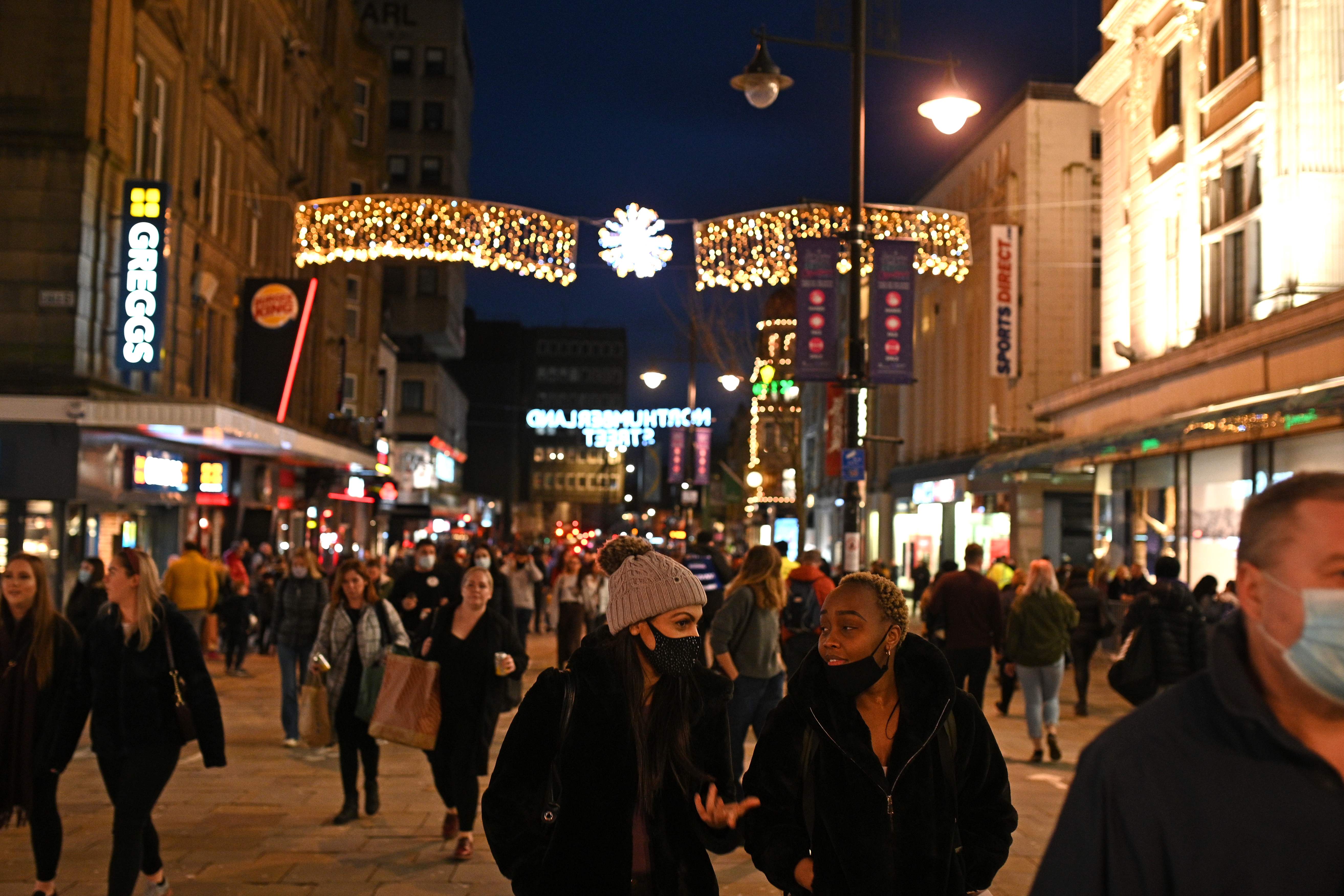 Pedestrians wearing protective face coverings to combat the spread of the coronavirus Covid-19 pandemic, walk through central Newcastle-upon-Tyne, in north-east England on December 19, 2020, on the last Saturday before Christmas. - British Prime Minister Boris Johnson on Wednesday resisted calls to tighten coronavirus restrictions over Christmas, as London faced stricter measures and concern grew about rising case numbers. The government has been under mounting pressure to toughen proposals allowing up to three households to meet indoors during a five-day festive window from December 23, as European neighbours curb their easing plans amid surging infections. (Photo by Oli SCARFF / AFP)