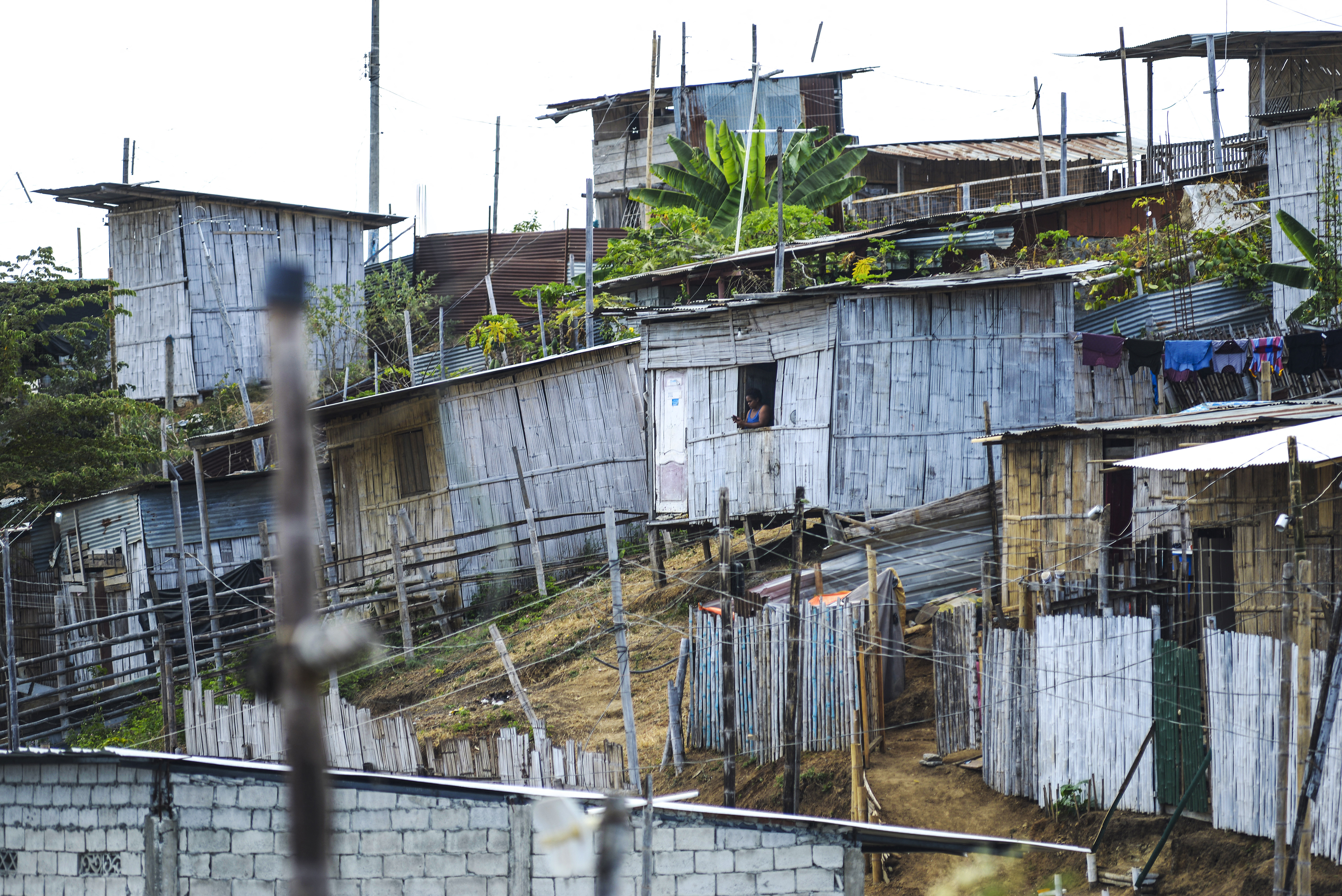 A woman looks out of the window of a house in the Ca�averal neighbourhood of the Ciudad de Dios cooperative in the Monte Sinai sector of Guayaquil, Ecuador, on July 26, 2022. - Without basic services, let alone schools and health centres, thousands of people are trapped in poverty in Ciudad de Dios populous settlement on the outskirts of Guayaquil, Ecuador's economic hub. (Photo by Marcos PIN / AFP)