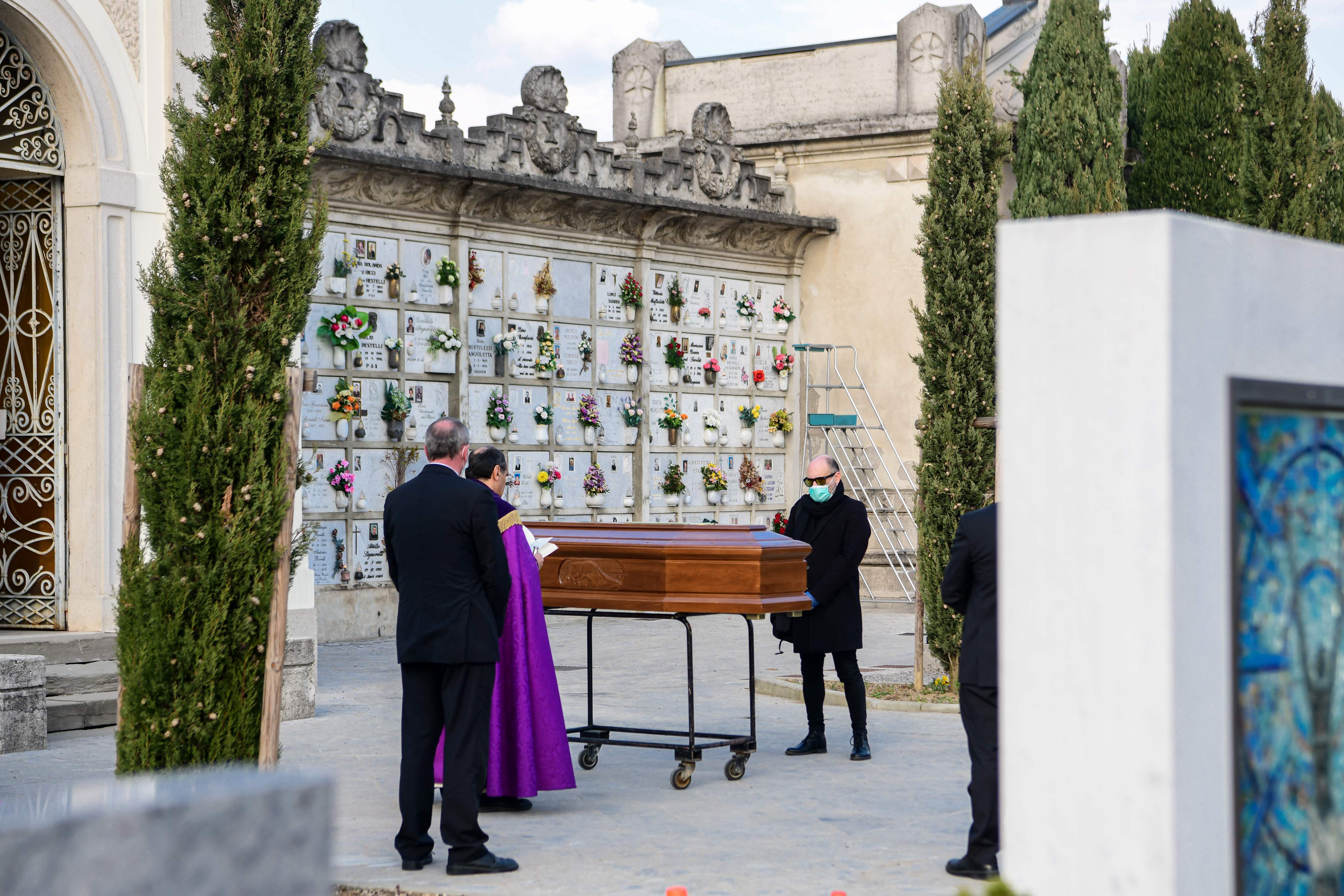 A man wearing a face mask (R) stands by the coffin of his mother as a priest (2ndL) reads prayers during a funeral service in the closed cemetery of Seriate, near Bergamo, Lombardy, on March 20, 2020 during the country's lockdown aimed at stopping the spread of the COVID-19 (new coronavirus) pandemic. (Photo by Piero Cruciatti / AFP)